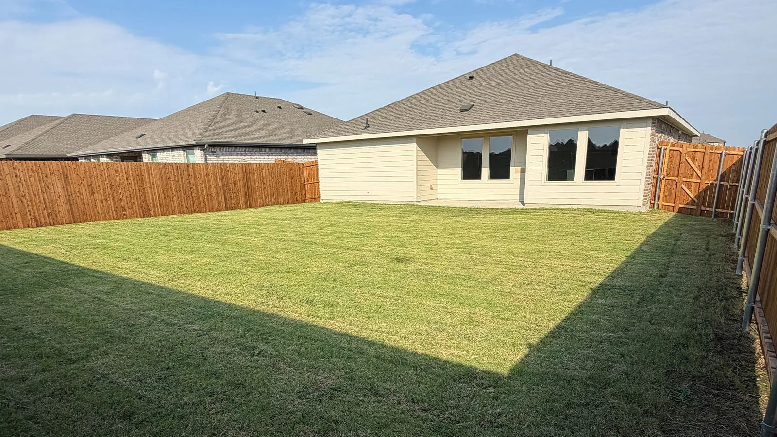 Expansive backyard featuring a manicured lawn, a full wood privacy fence, and a rear exterior with multiple windows