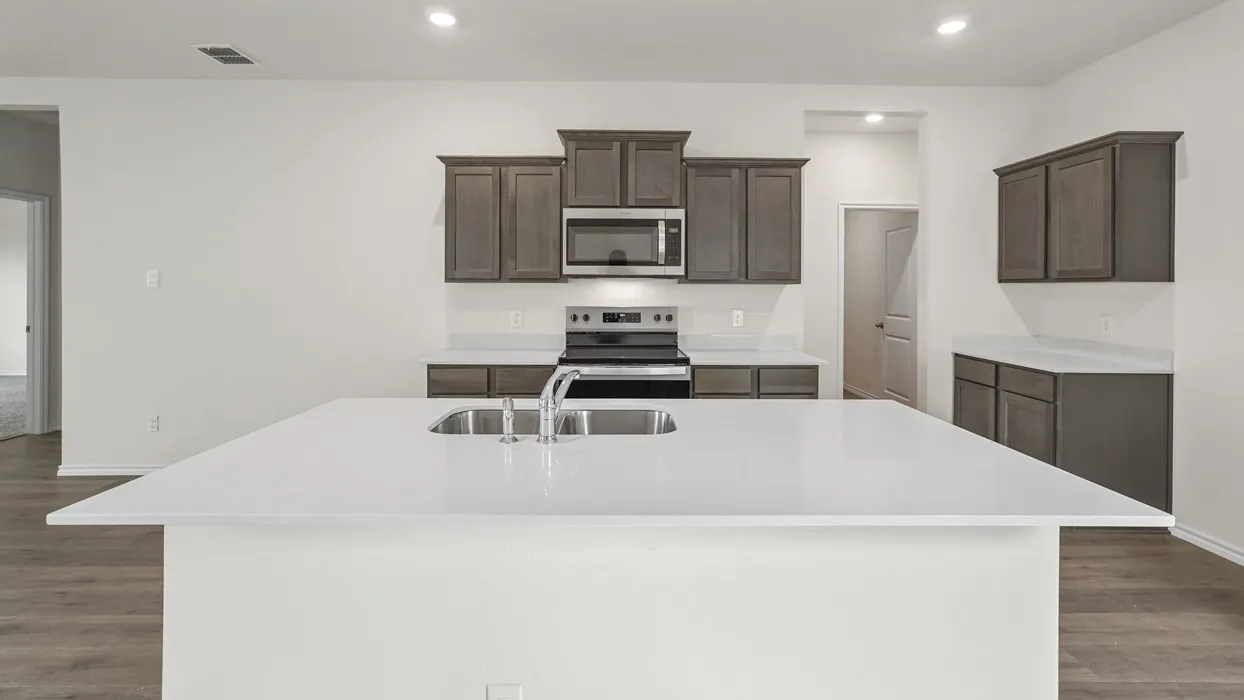 Spacious kitchen island with a built-in sink, stainless steel faucet, white countertops, gray wood-finish cabinetry, and wood-finish flooring