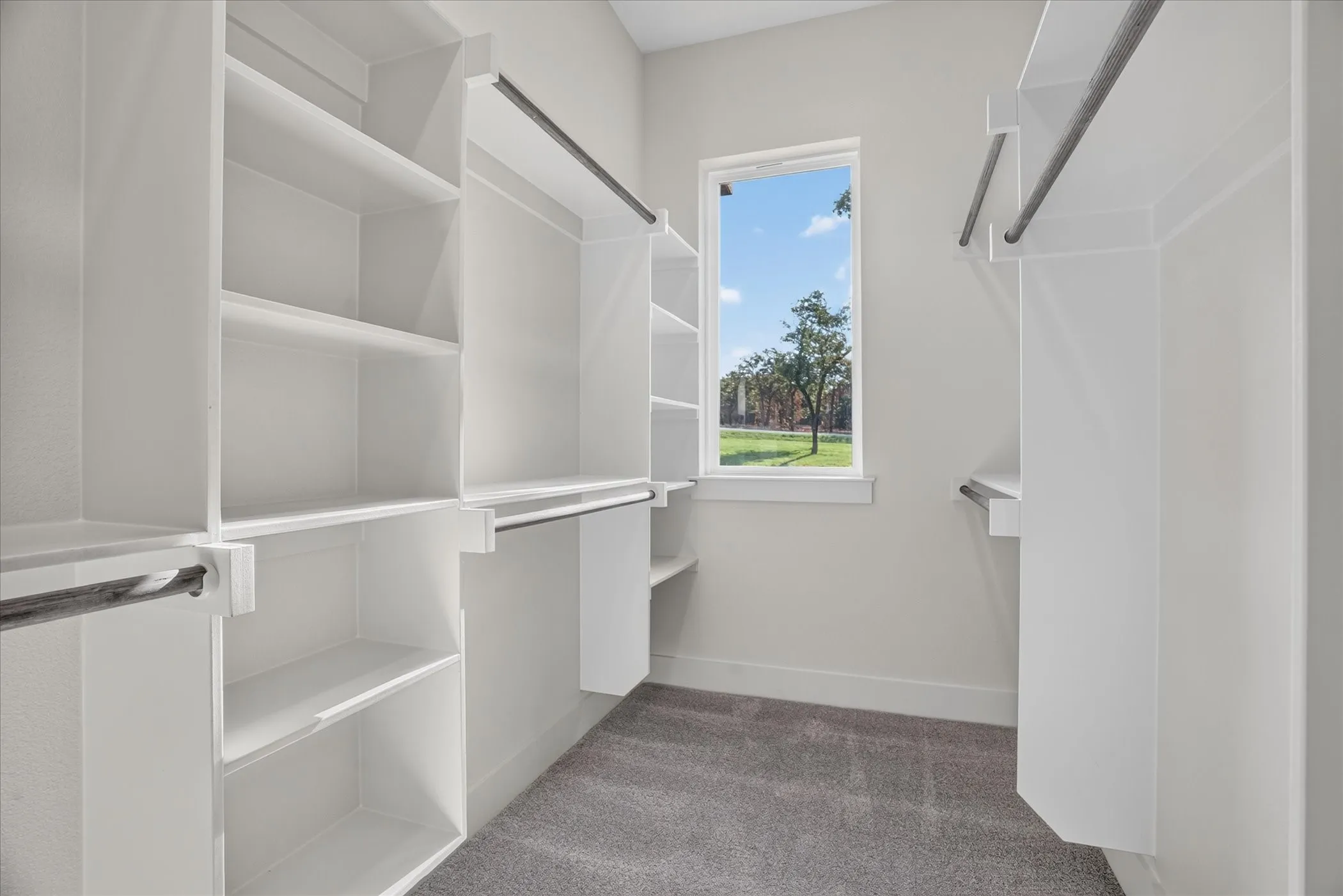 Built-in white shelving, integrated hanging rods, a single window, and gray carpeting