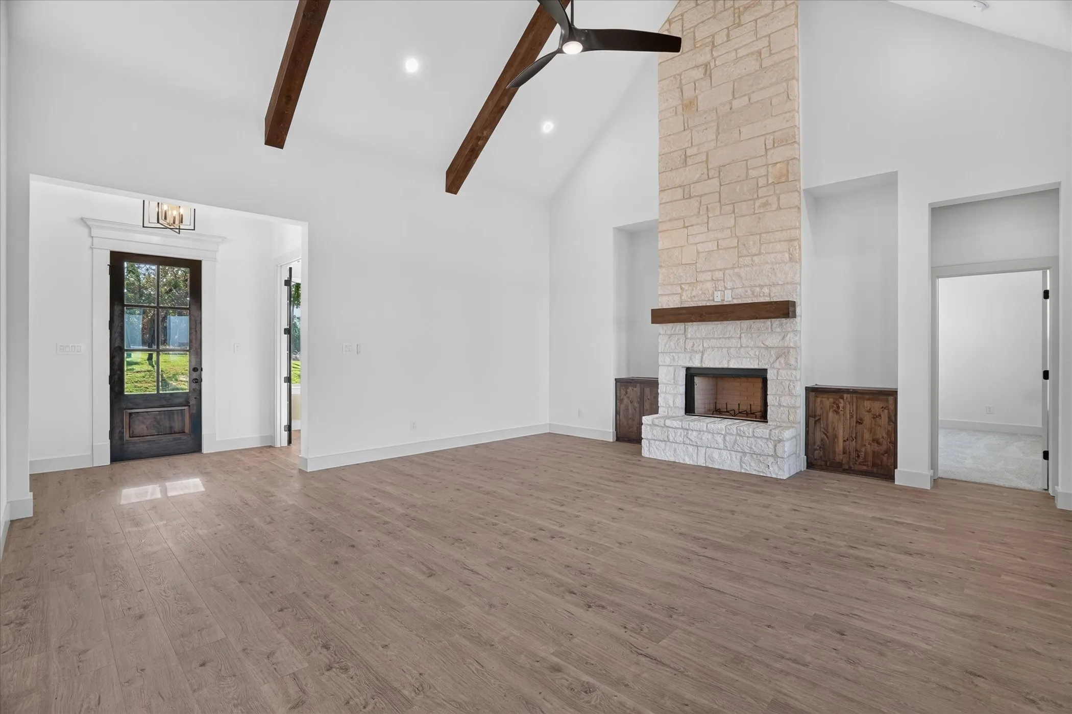Vaulted ceiling with exposed wood beams, stone fireplace with wood mantel, wood-finish flooring, recessed lighting, and a dark wood-paneled door