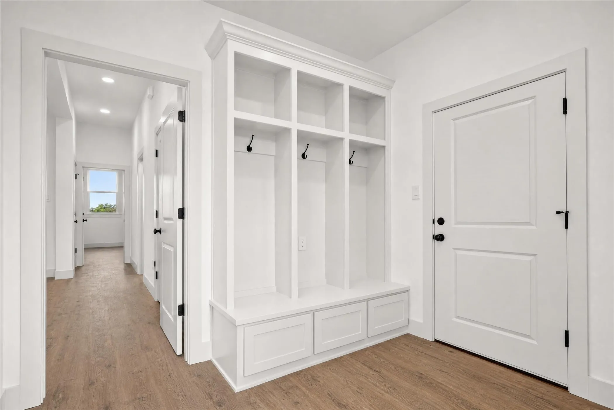 Built-in storage with coat hooks and base cabinetry, wood-finish flooring, recessed lighting, and white paneled doors with black hardware