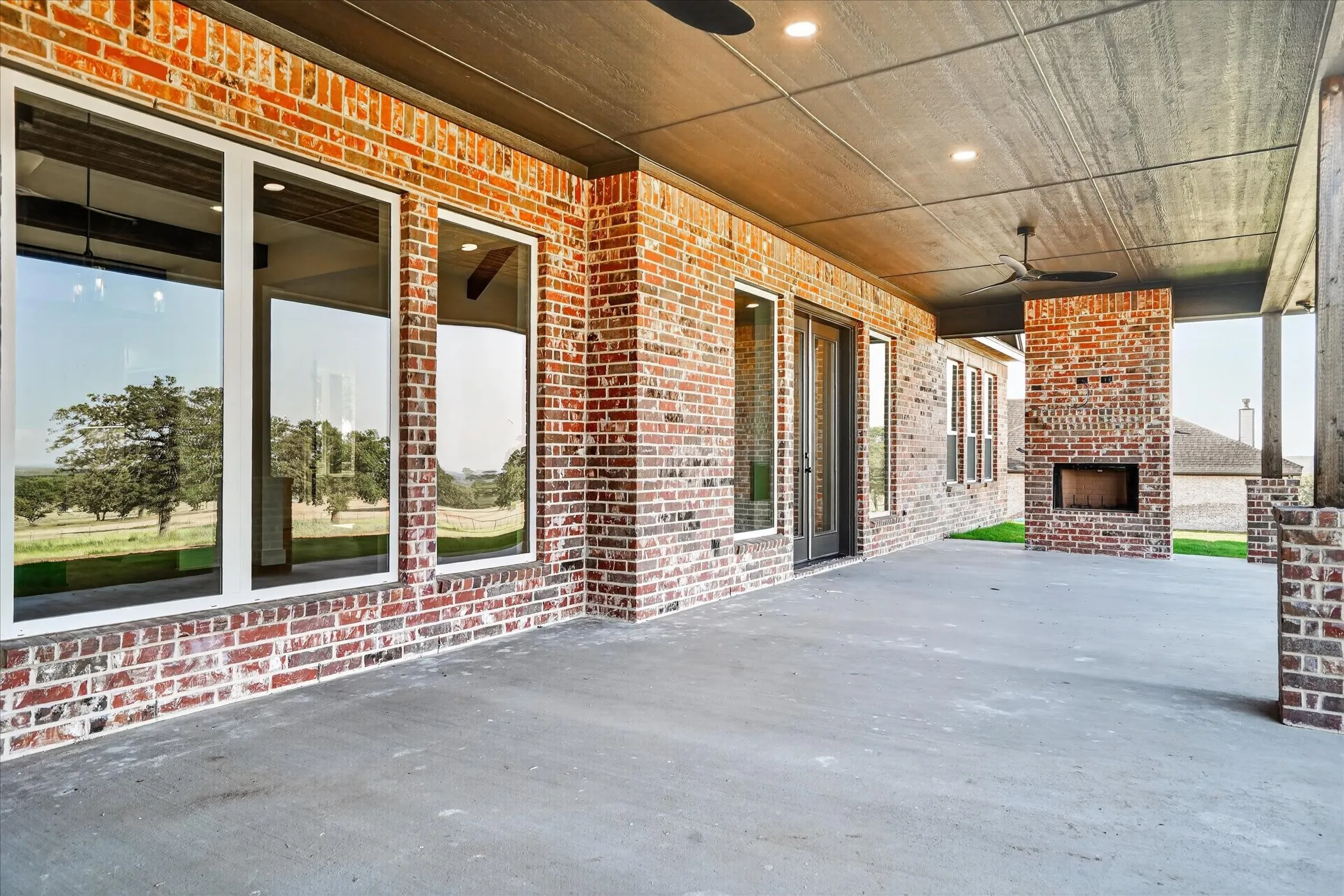 Covered patio with a brick exterior, outdoor fireplace, and concrete flooring