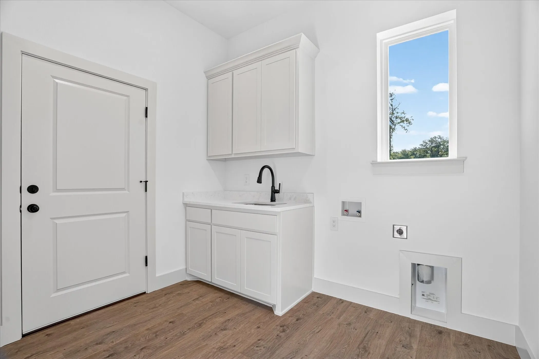 Wood-finish flooring, white paneled cabinetry, countertop with integrated sink, matte black faucet, and a large window