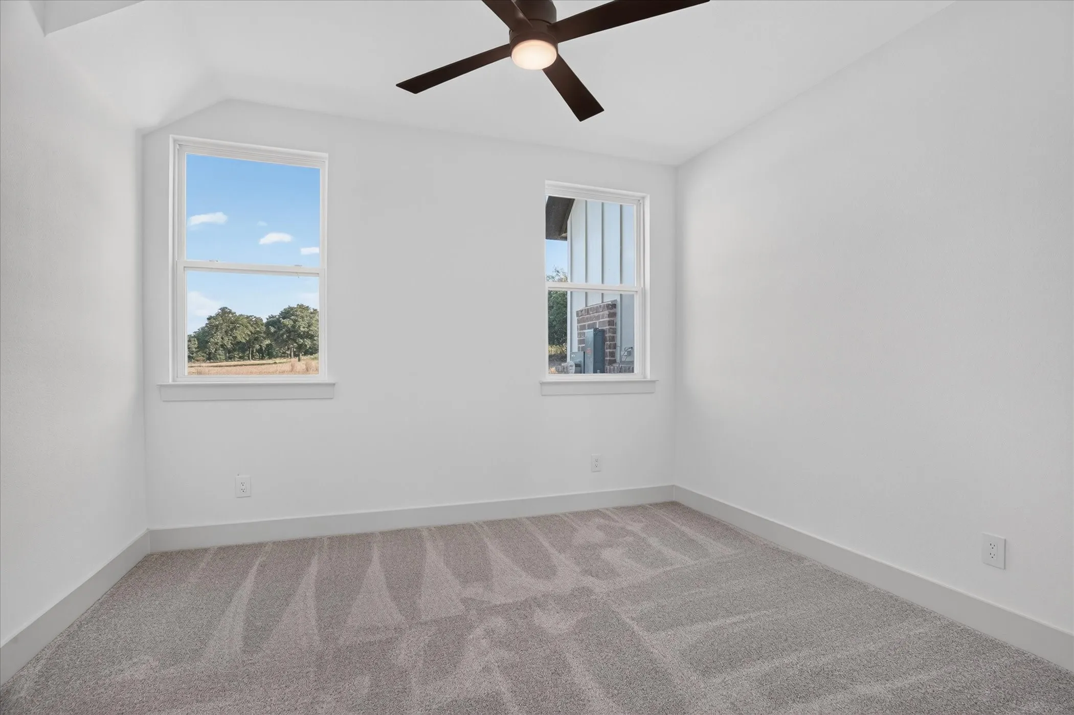 Vaulted ceiling with a ceiling fan, white walls, two white-framed windows, and gray carpet flooring