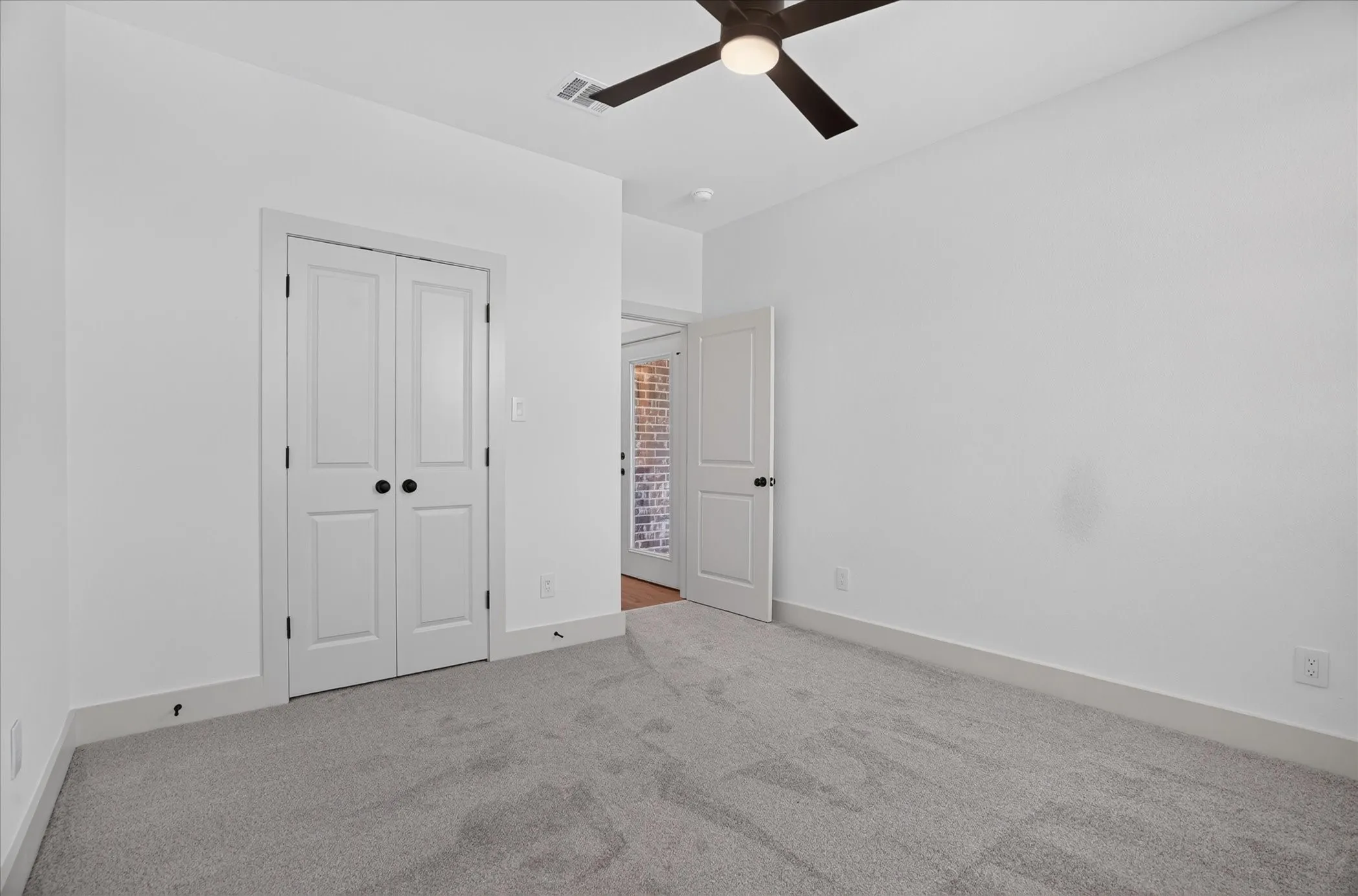 Neutral tone walls, grey carpet, ceiling fan with integrated lighting, white trim, and white doors with matte black hardware