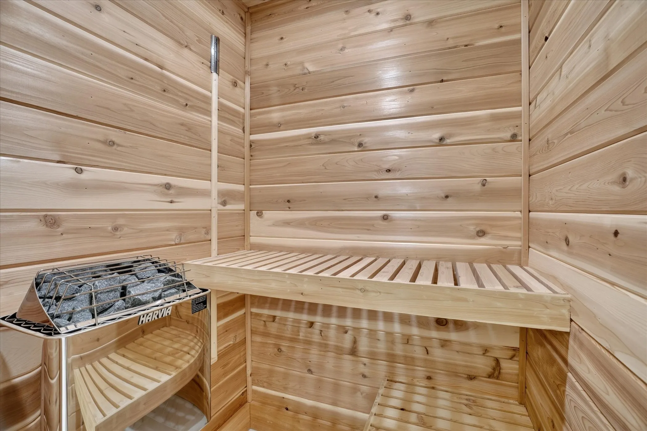 Cedar-paneled sauna featuring a built-in slatted bench and a Harvia sauna heater with rocks