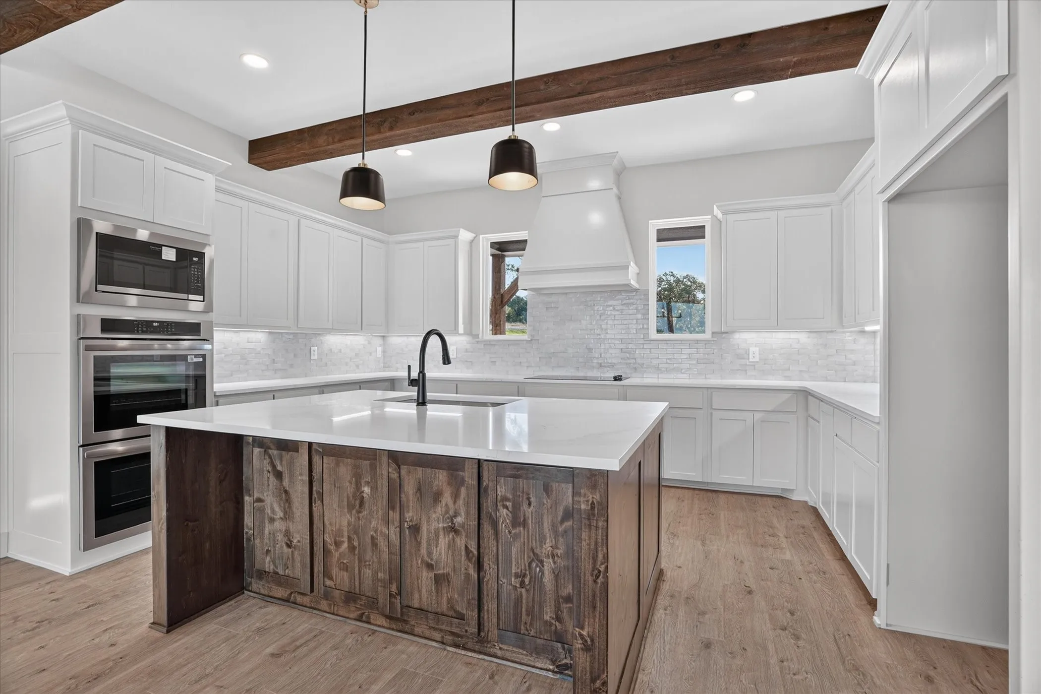 Kitchen featuring white cabinetry, wood-finish flooring, a wood beam ceiling accent, a center island with a white countertop, and stainless steel built-in appliances