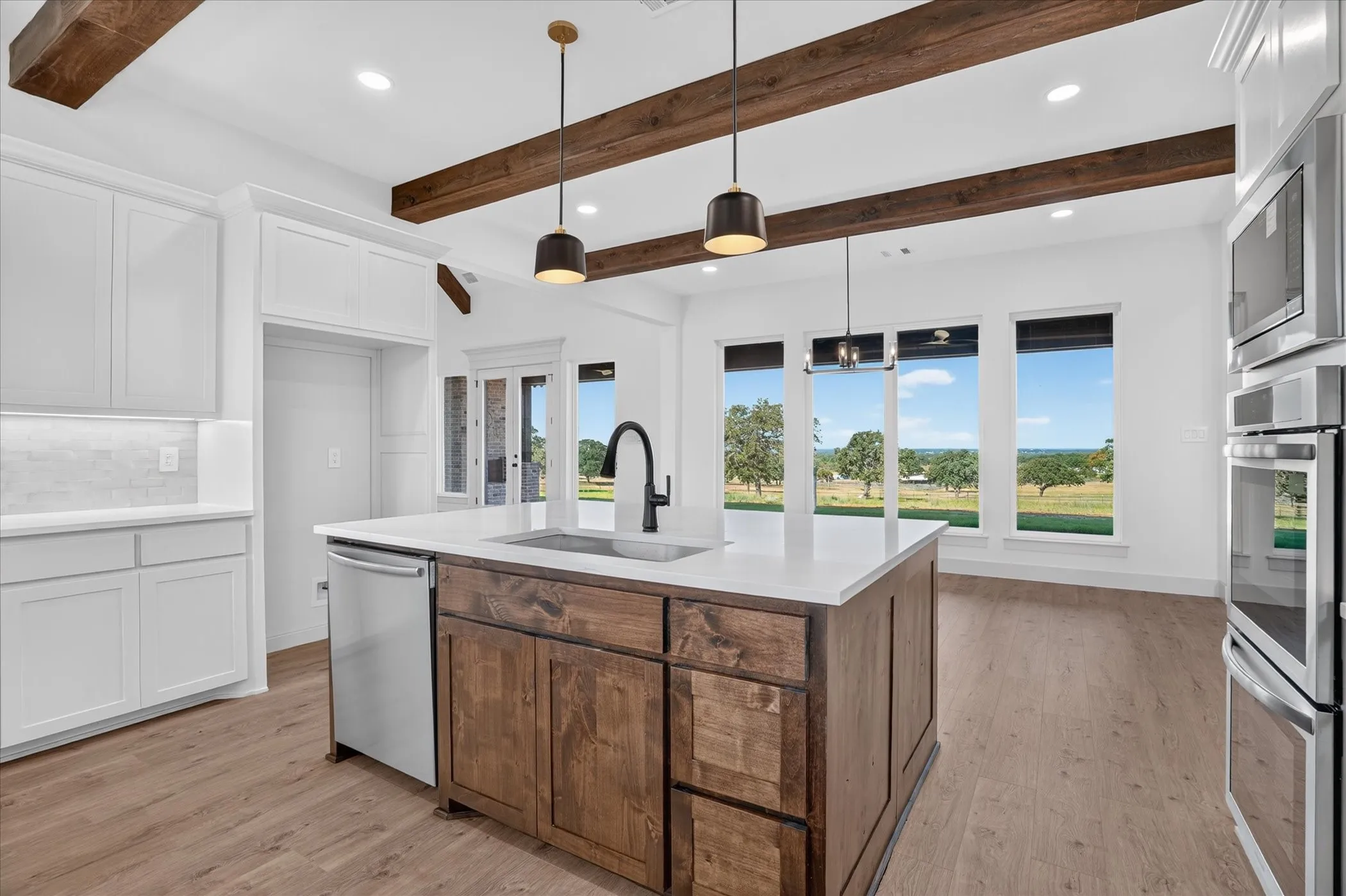 Open-concept kitchen with wood-finish flooring, white cabinetry, a large center island, and stainless steel appliances
