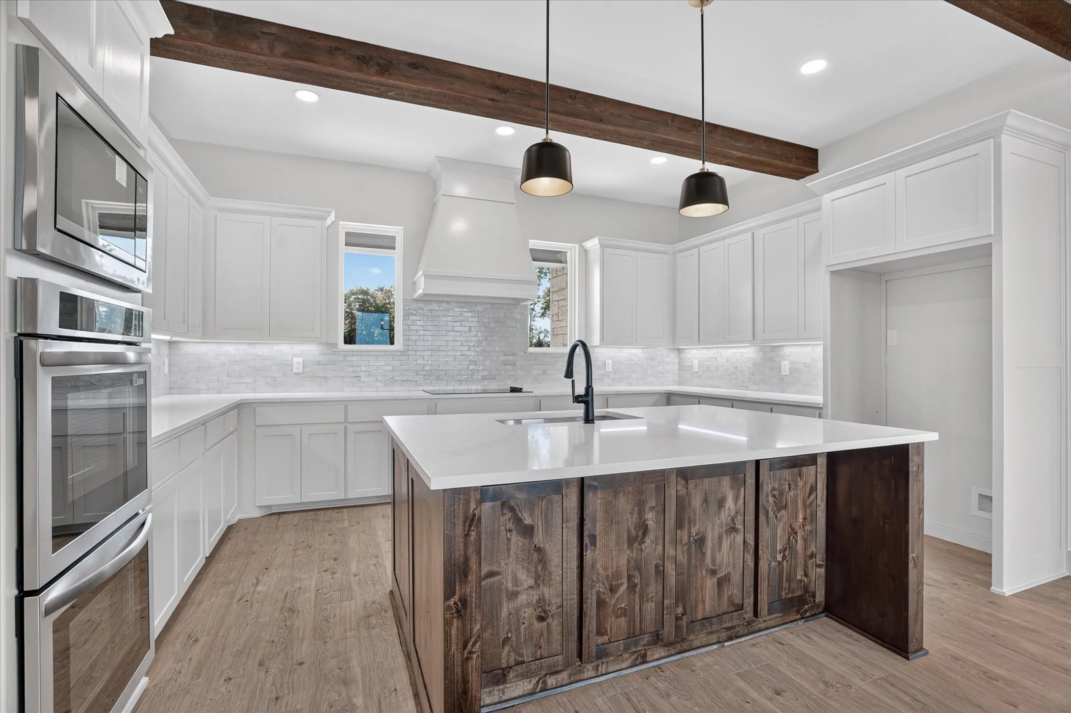 Modern kitchen featuring white cabinetry, a wood-finish island with a sink, stainless steel built-in appliances, and overhead wood beams