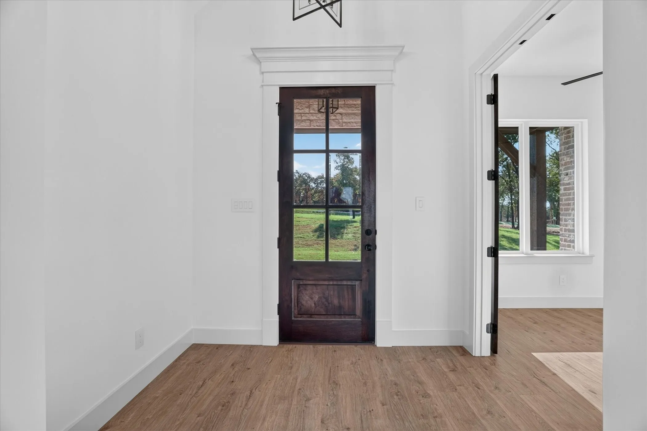 Wood-finish flooring, white trim, and a dark wood-finish door with glass panels