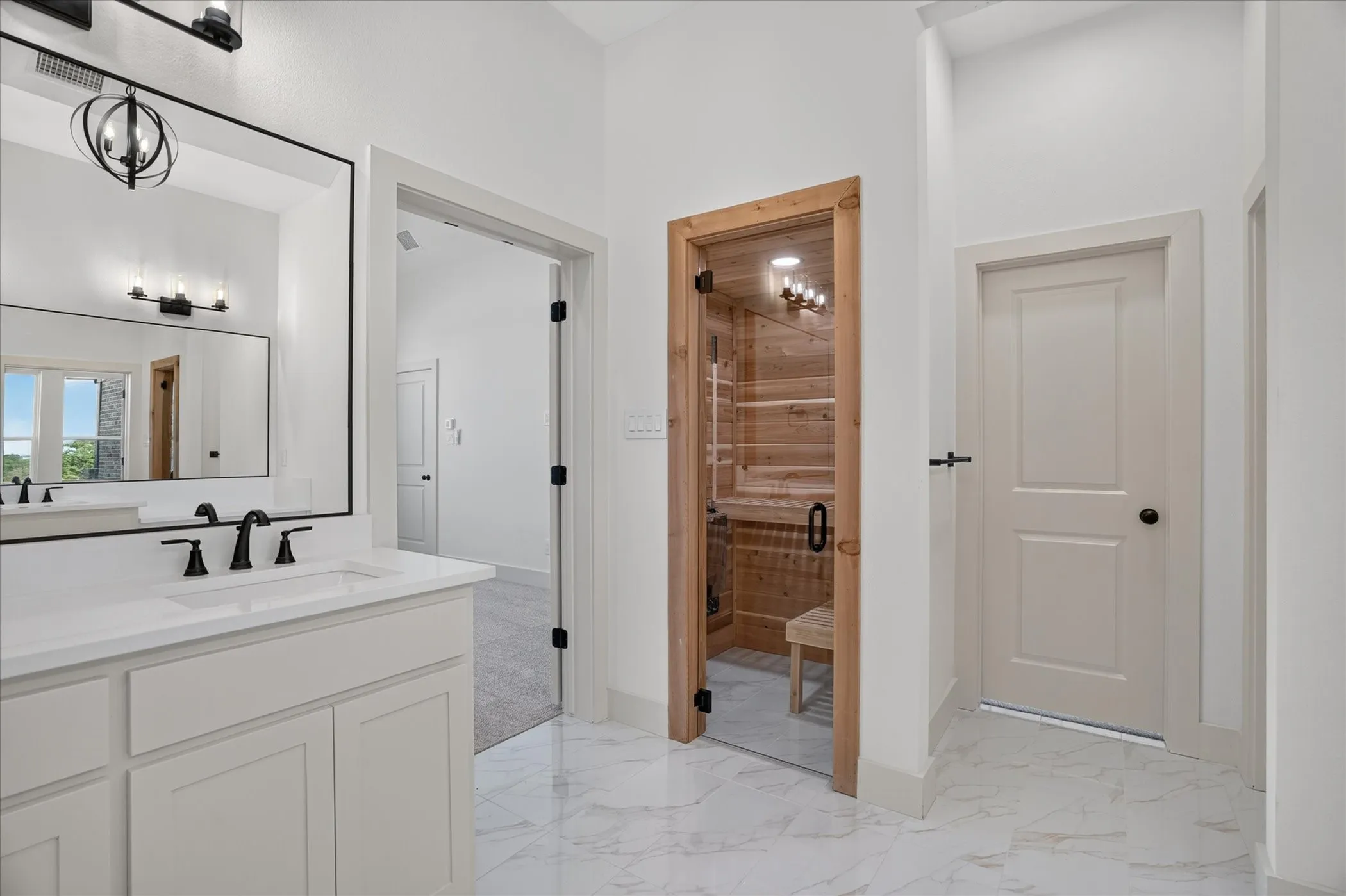White vanity with integrated sink and matte black fixtures, framed mirror, and marble-look floor tile