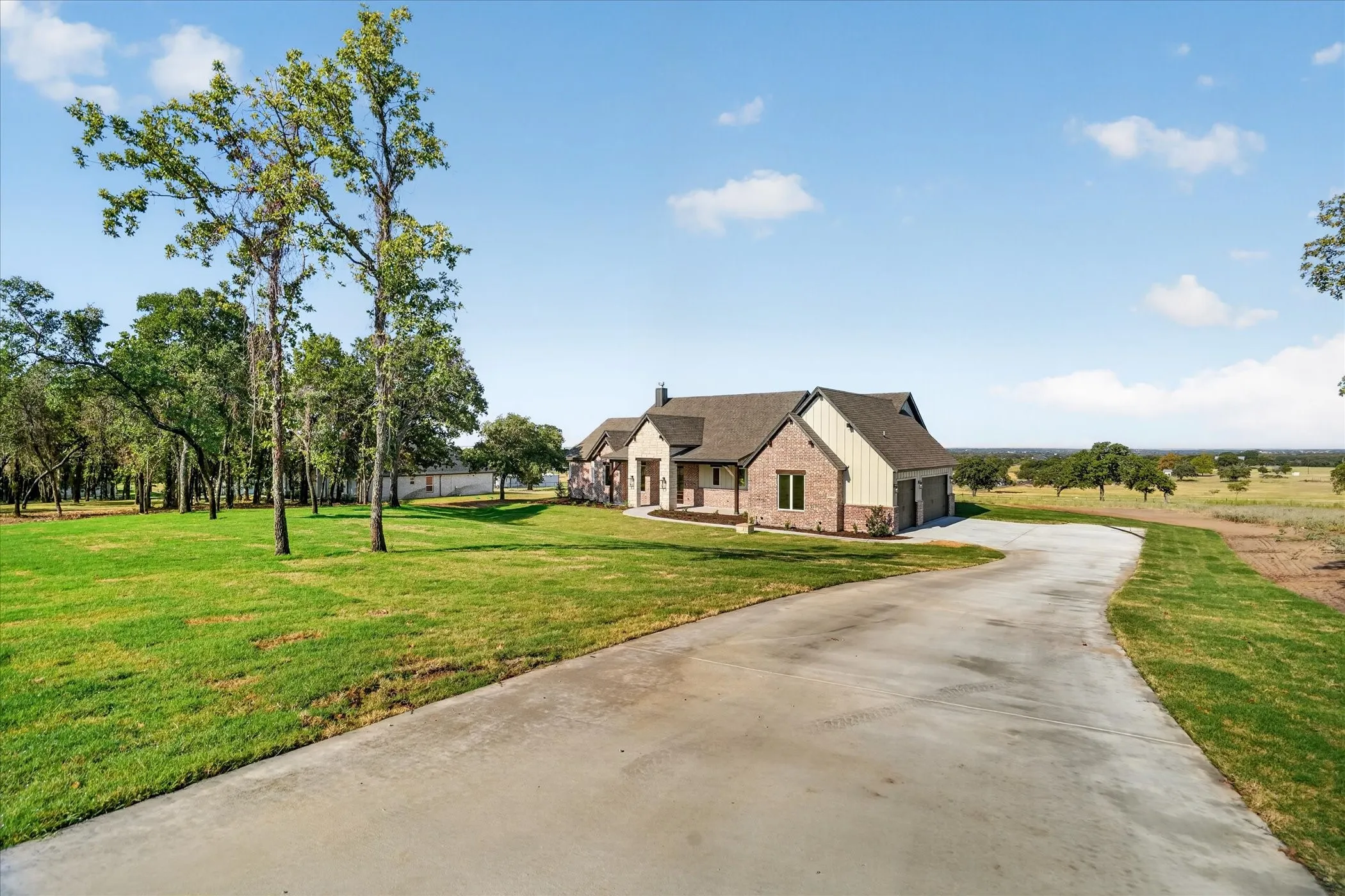 Brick and siding exterior, concrete driveway, attached garage, gabled roofline, mature trees, and expansive lawn