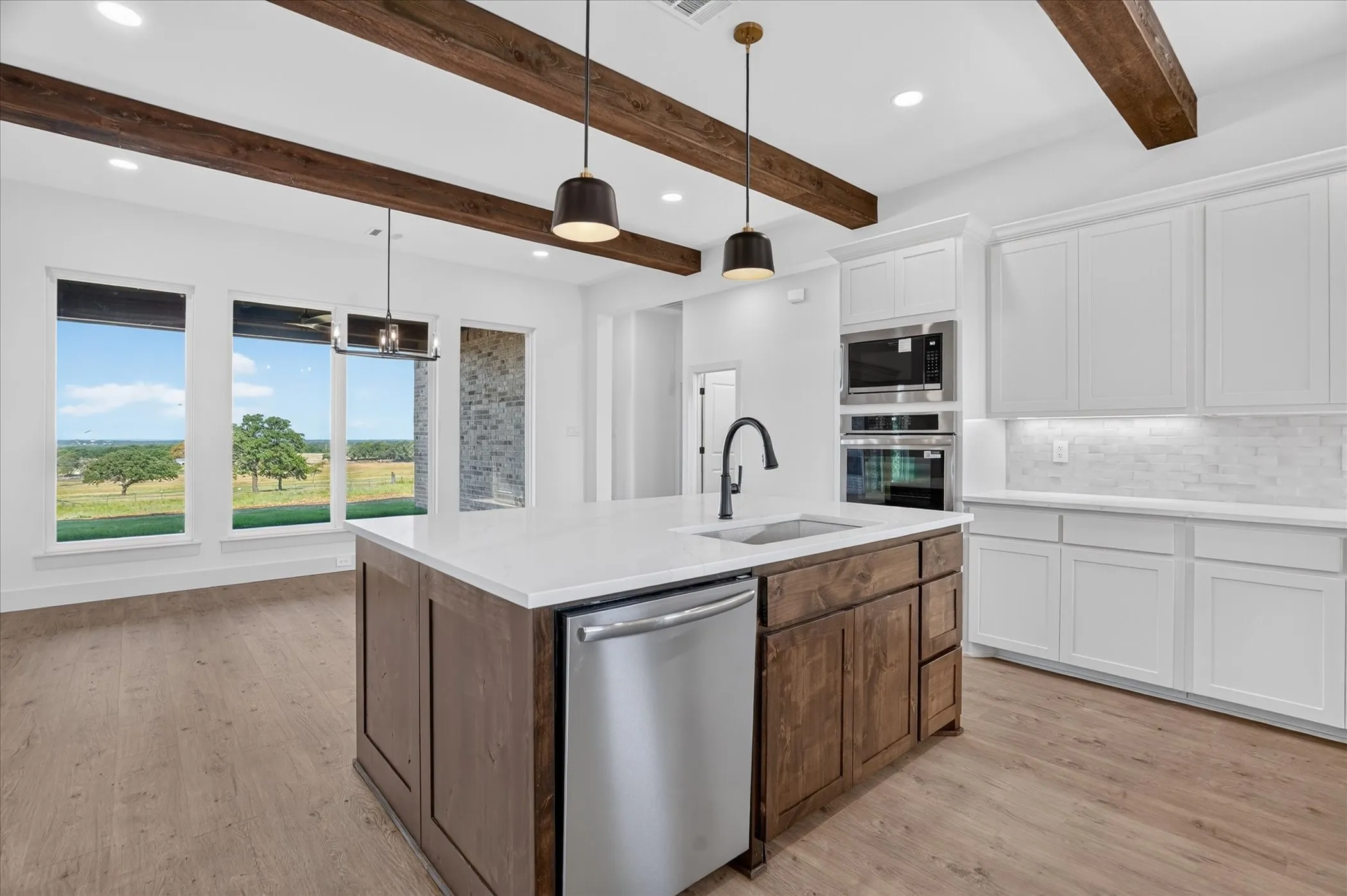 Gourmet kitchen featuring a center island with sink, stainless steel appliances, wood-finish flooring, white cabinetry, and exposed ceiling beams