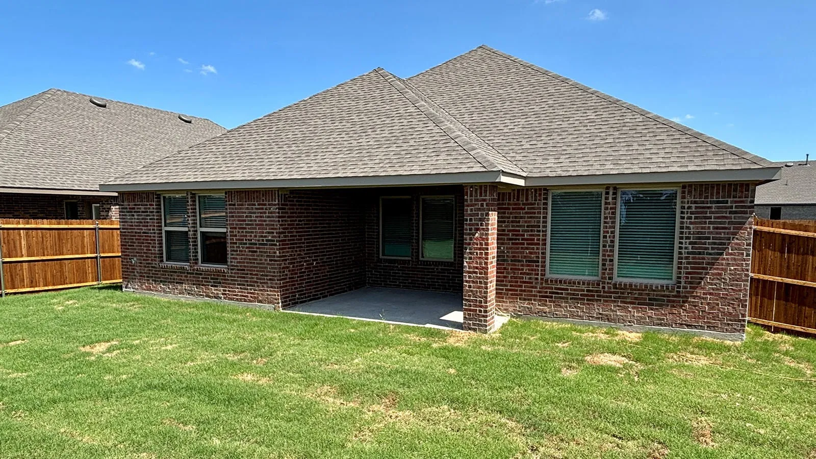 Brick exterior with shingle roof, covered patio, and wood fencing