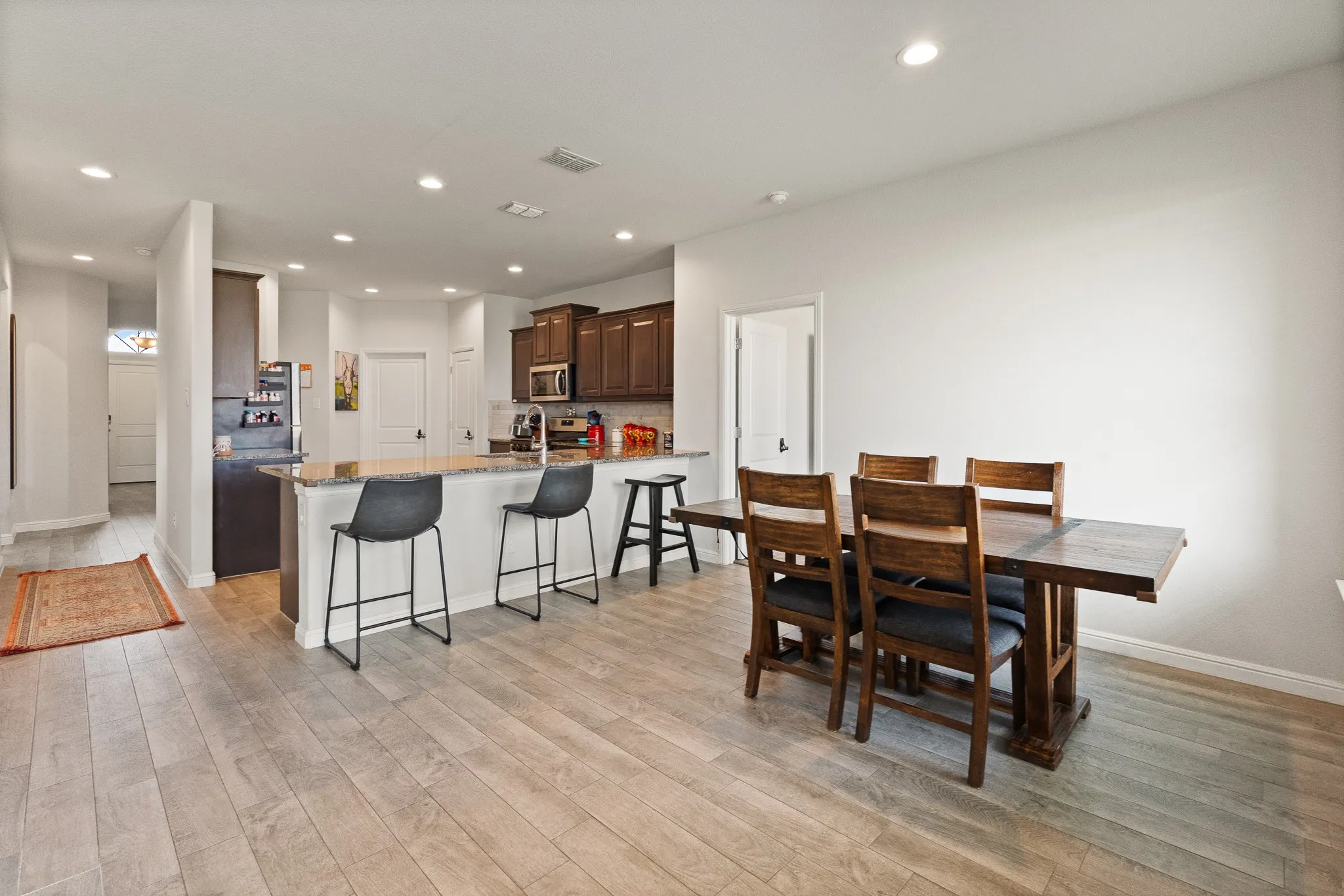 Recessed lighting, wood-finish flooring, kitchen island with seating, built-in microwave, and dark wood-finish cabinetry