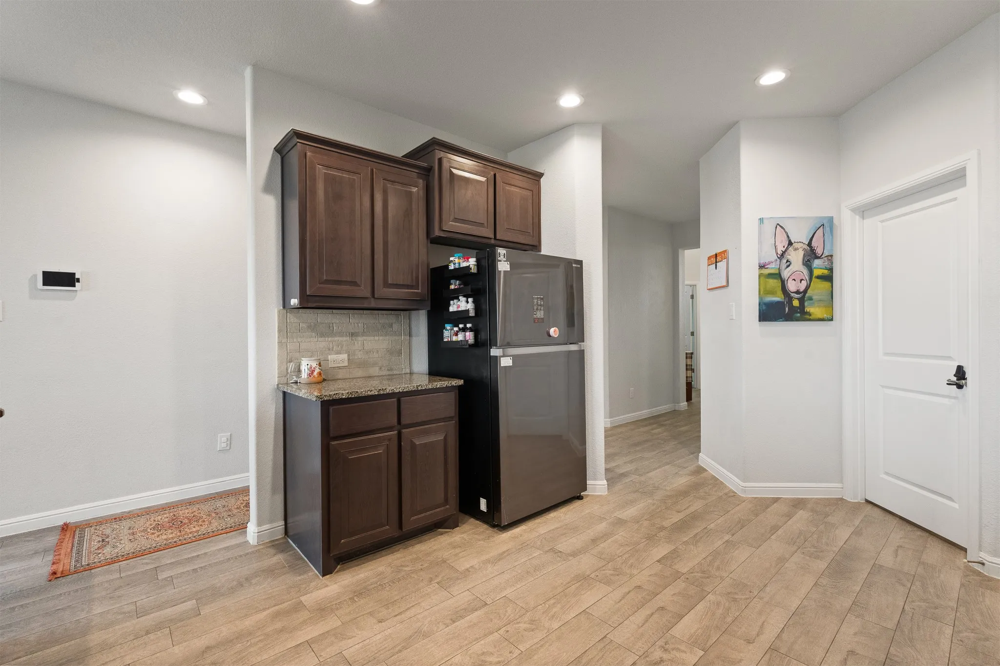 Wood-finish flooring, recessed lighting, dark wood-finish cabinetry, light-toned backsplash, and a solid surface countertop