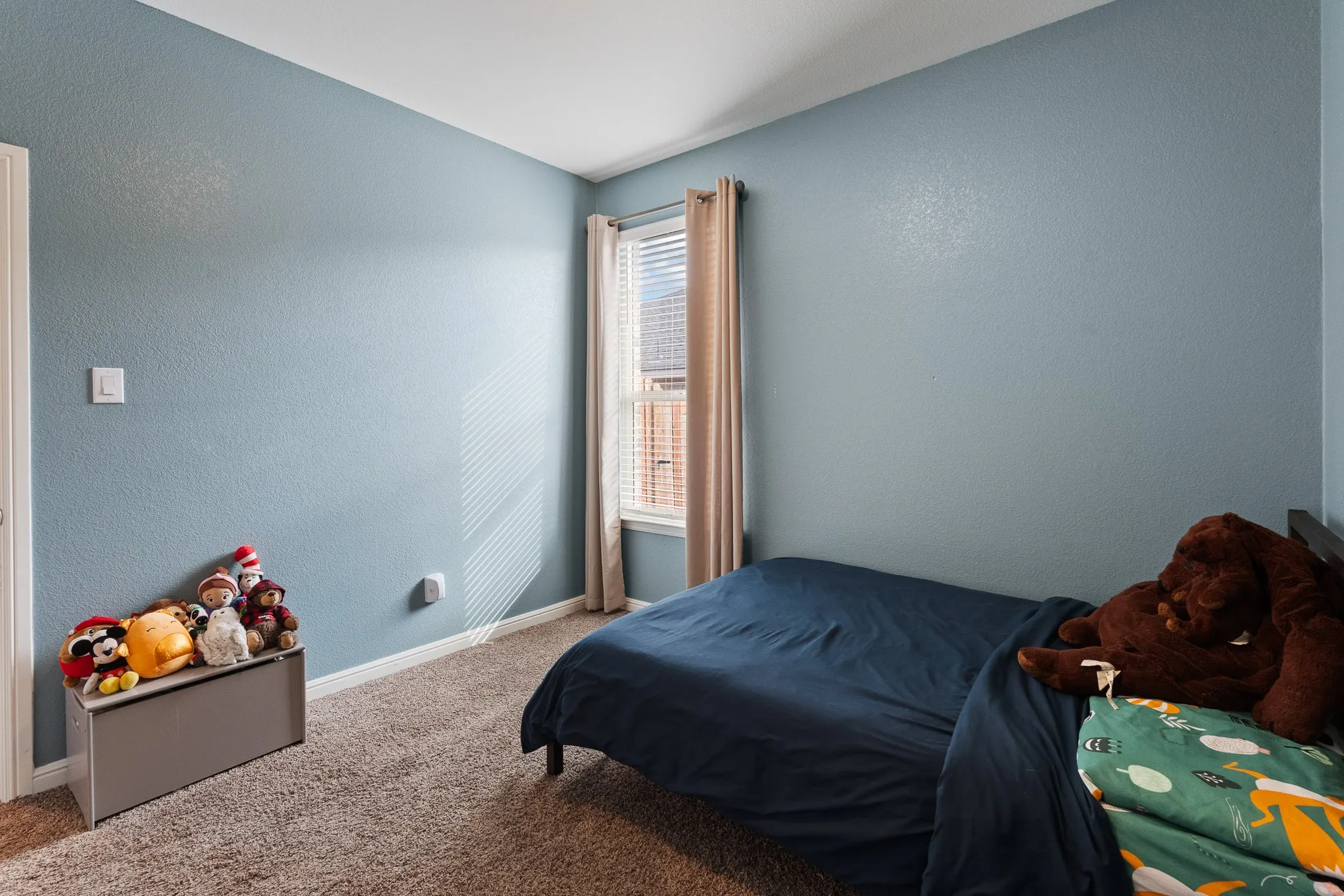 Textured walls in a light blue finish, carpeted flooring, and a window with blinds