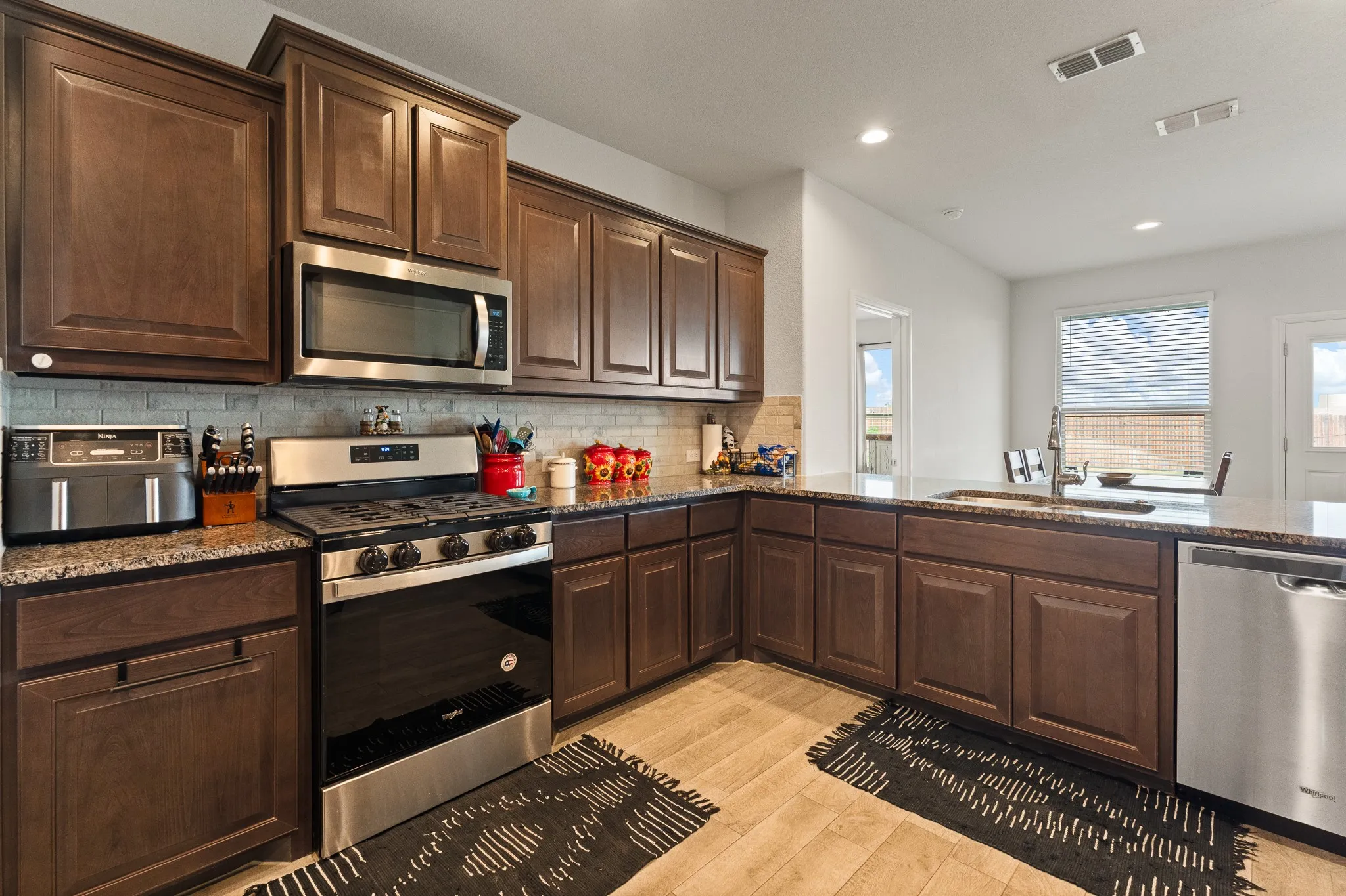 Expansive kitchen featuring wood-finish cabinetry, granite countertops, a tile backsplash, and stainless steel appliances, including an oven/range, microwave, and dishwasher