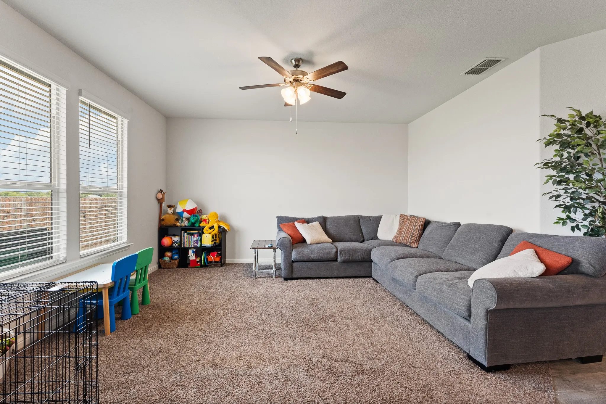 Carpeted flooring, white walls, two large windows with blinds, and a ceiling fan with integrated lighting