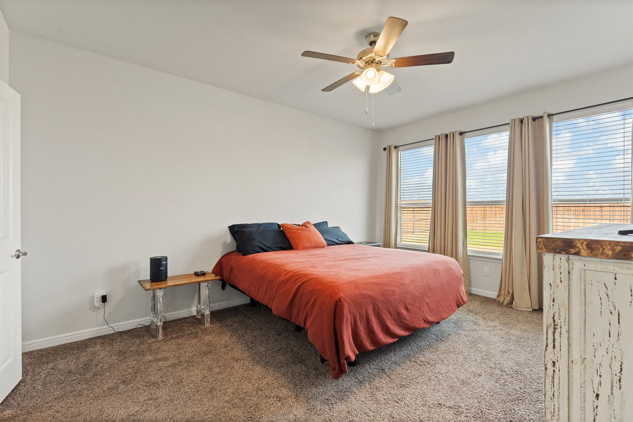 Plush carpeting, ceiling fan with integrated lighting, three large windows, and a classic paneled door