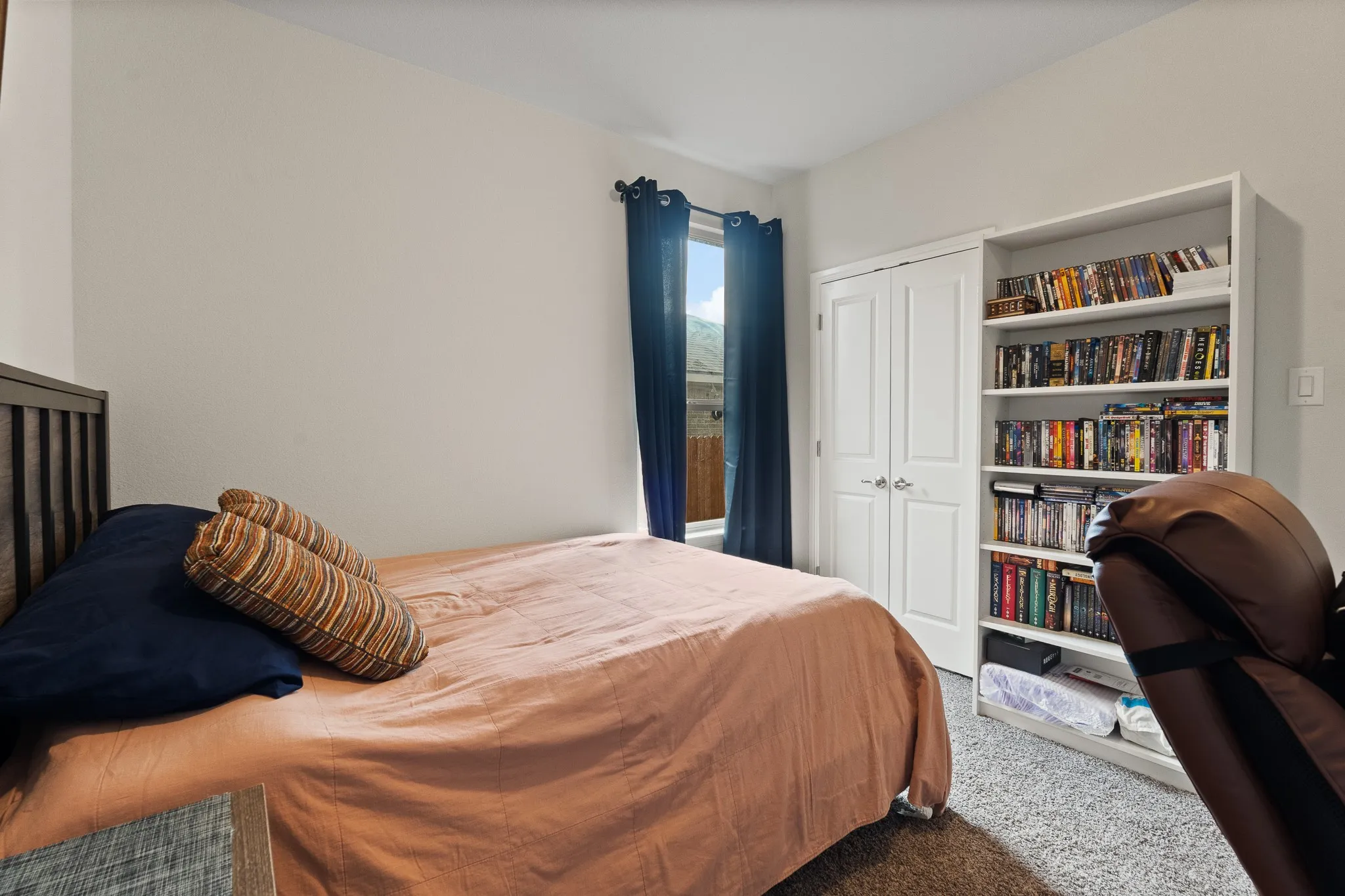Built-in shelving, white double-door closet, window with dark drapes, light neutral wall paint, and gray carpet