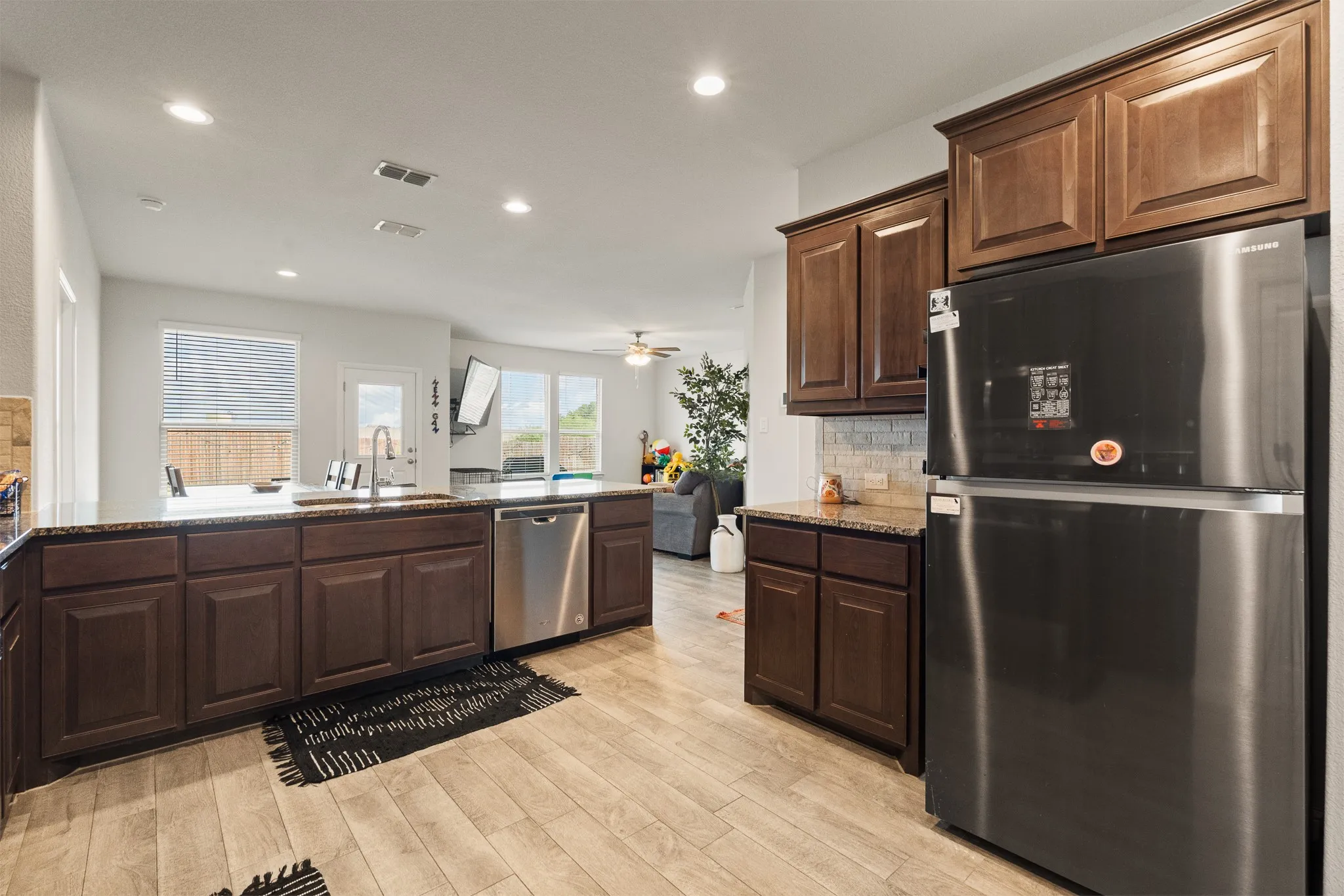 Kitchen featuring wood-finish flooring, dark wood cabinetry, light-toned countertops, a stainless steel dishwasher, and a stainless steel refrigerator