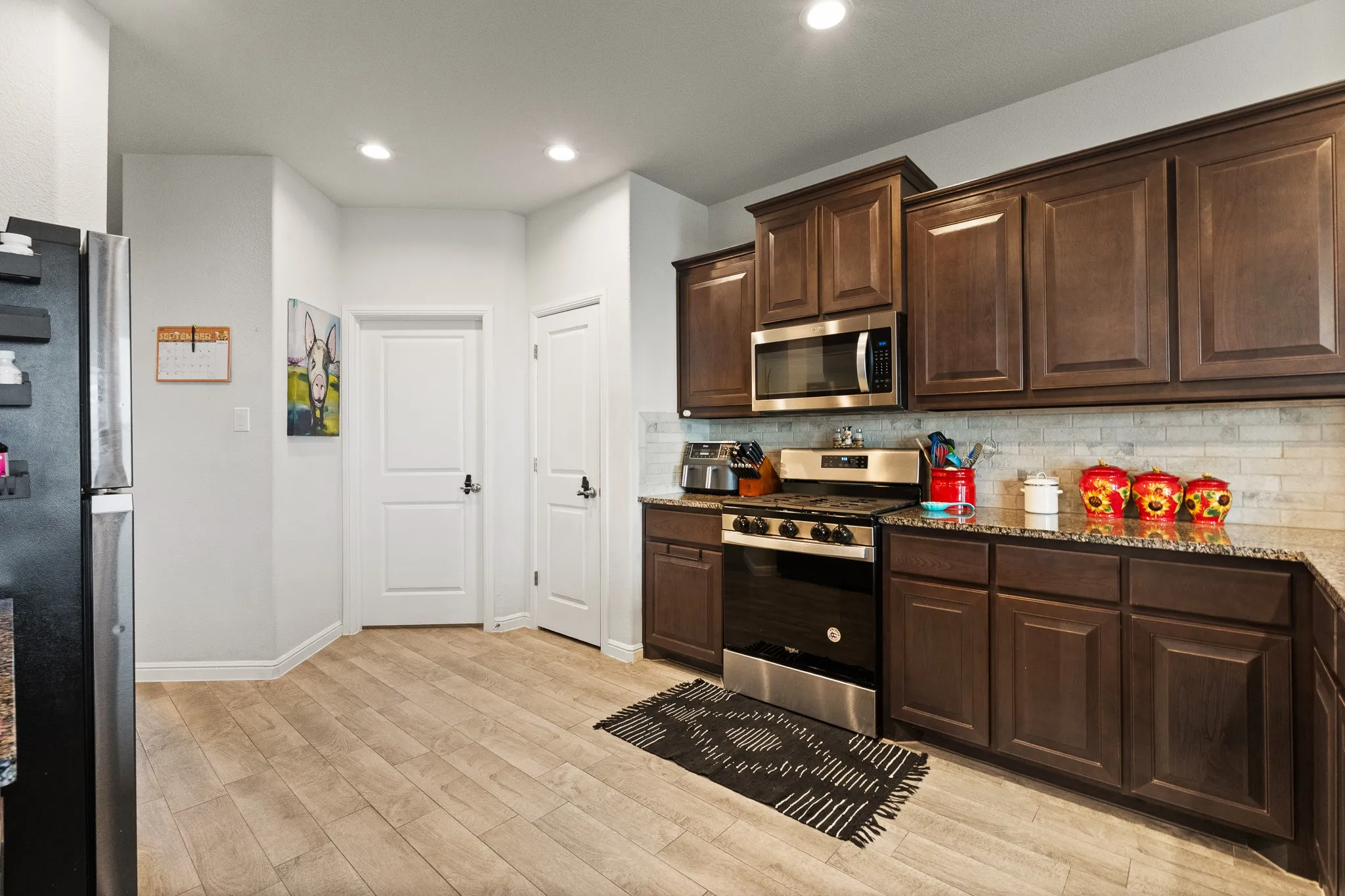 Kitchen featuring wood-finish flooring, dark wood cabinetry, a built-in microwave, a stainless steel range, and stone countertops