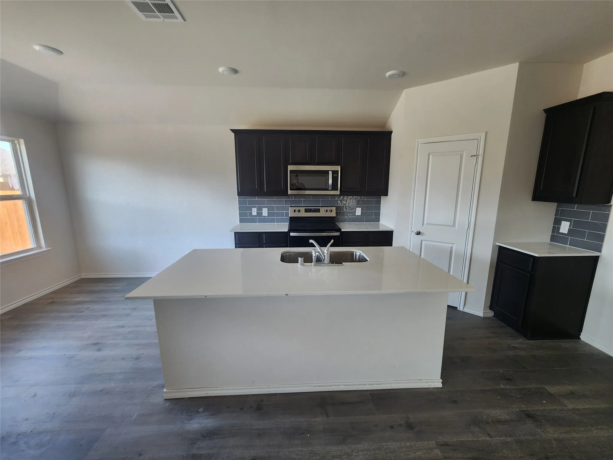 Spacious kitchen featuring dark cabinetry, subway tile backsplash, white countertops, and wood-finish flooring