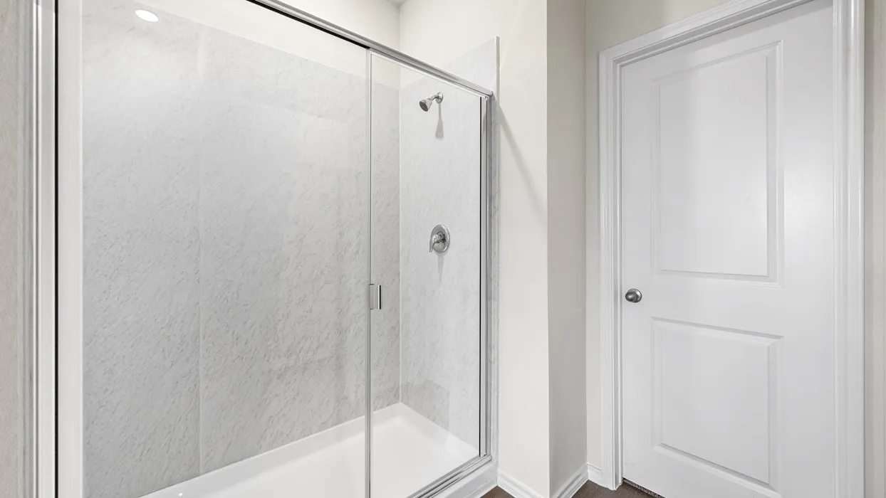 Shower enclosure with clear glass sliding doors, textured shower surround, chrome shower fixtures, and a white paneled door