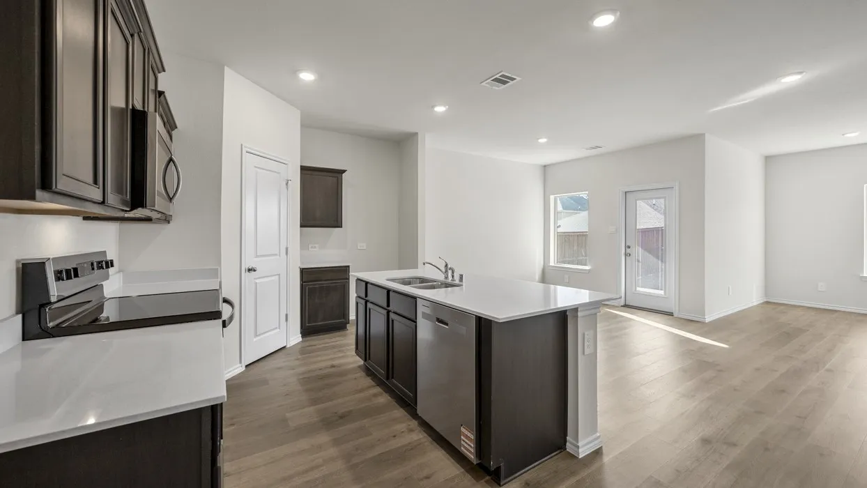 Kitchen featuring dark wood-finish cabinetry, light countertops, an undermount sink, and stainless steel appliances