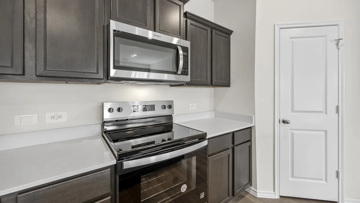 Dark wood-finish cabinetry, stainless steel microwave, stainless steel electric range, light-toned countertops, and a paneled interior door