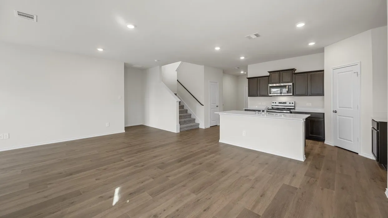 Open-concept living space featuring wood-finish flooring throughout, recessed ceiling lighting, and a curved architectural staircase
