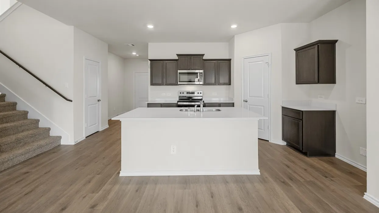 Kitchen featuring dark wood-finish cabinetry, white countertops, a stainless steel microwave, and a kitchen island with an integrated sink