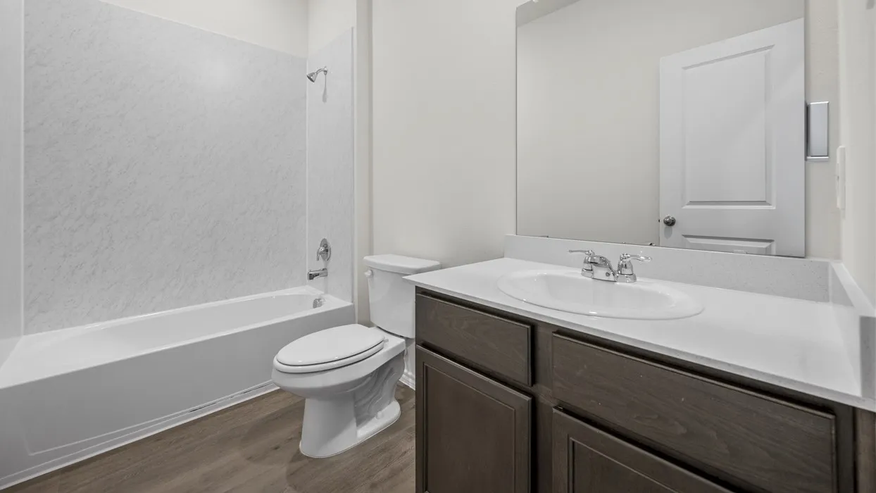 Bathroom featuring a full vanity with a white countertop and wood-finish cabinetry, a white toilet, and a white bathtub with a shower and surround
