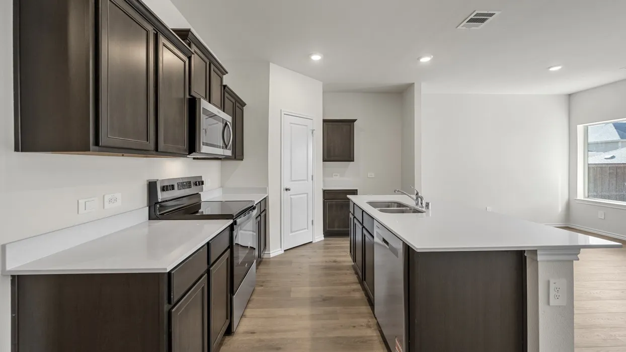 Galley-style kitchen featuring dark cabinetry with contrasting white quartz countertops, stainless steel appliances including a built-in microwave and range, wood-finish flooring throughout, and recessed ceiling lighting