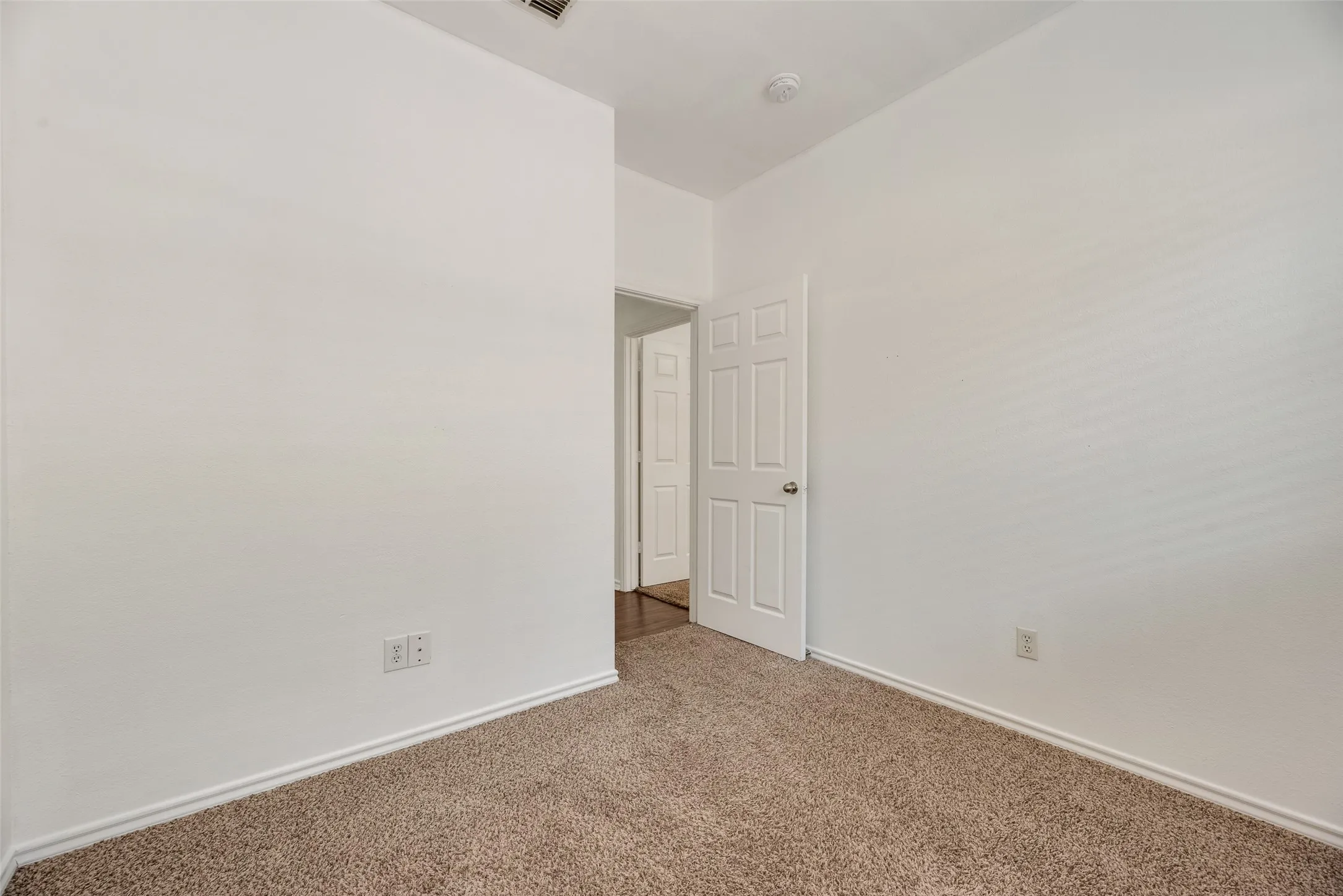 White painted walls, neutral carpet flooring, and a white paneled door