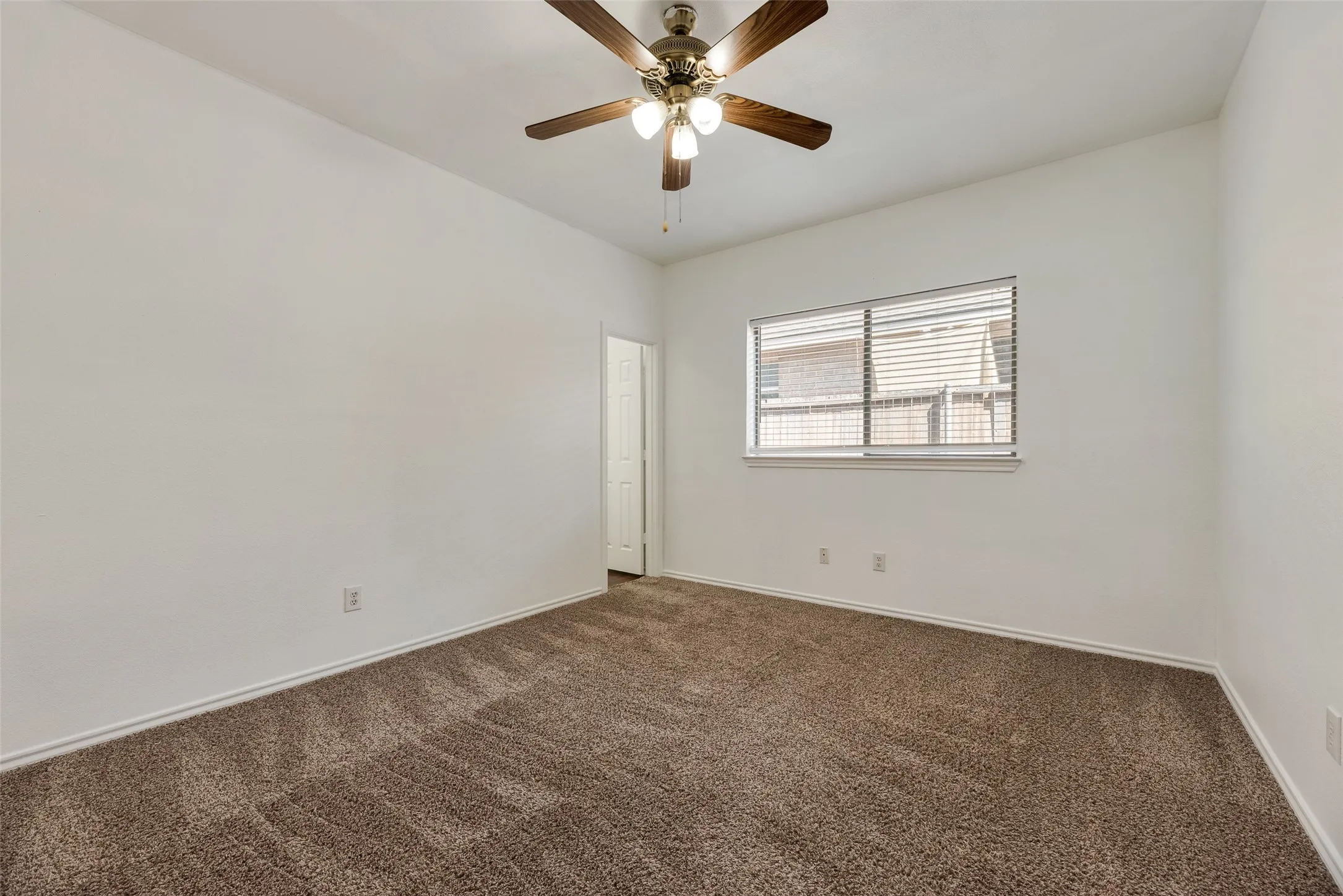 Spacious room featuring neutral paint, brown carpet flooring, and a ceiling fan with integrated lighting