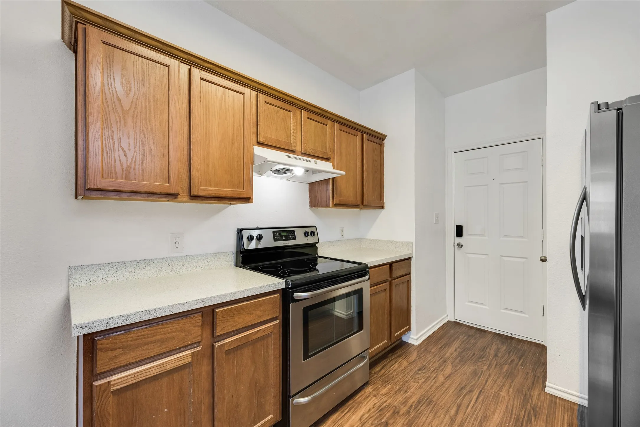 Wood-finish flooring, stainless steel range, light-toned countertops, and wood cabinetry