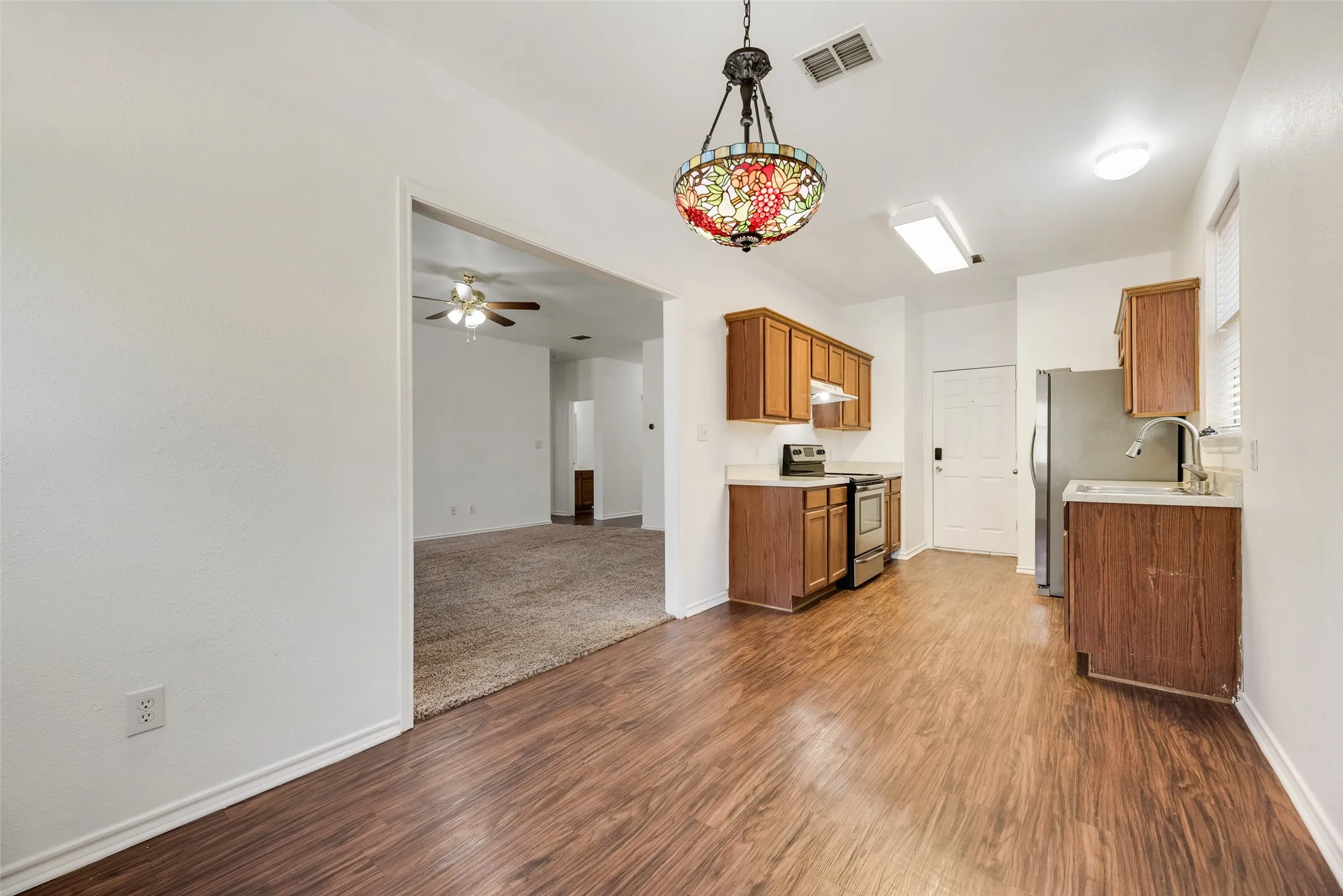 Wood-finish flooring, wood cabinetry, stainless steel appliances, and a stained glass light fixture