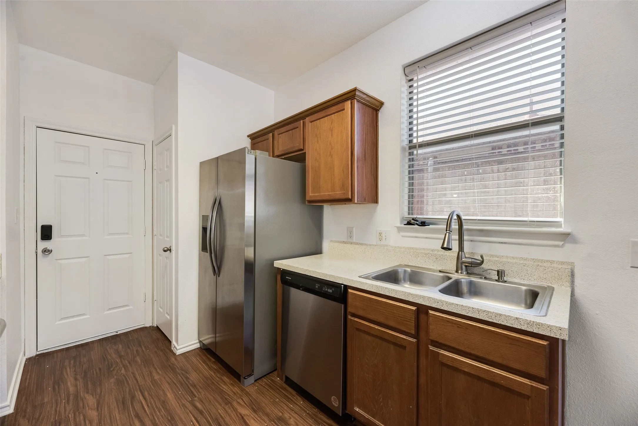 Wood-finish flooring, stainless steel appliances, dual basin sink, light-toned countertops, and wood cabinetry