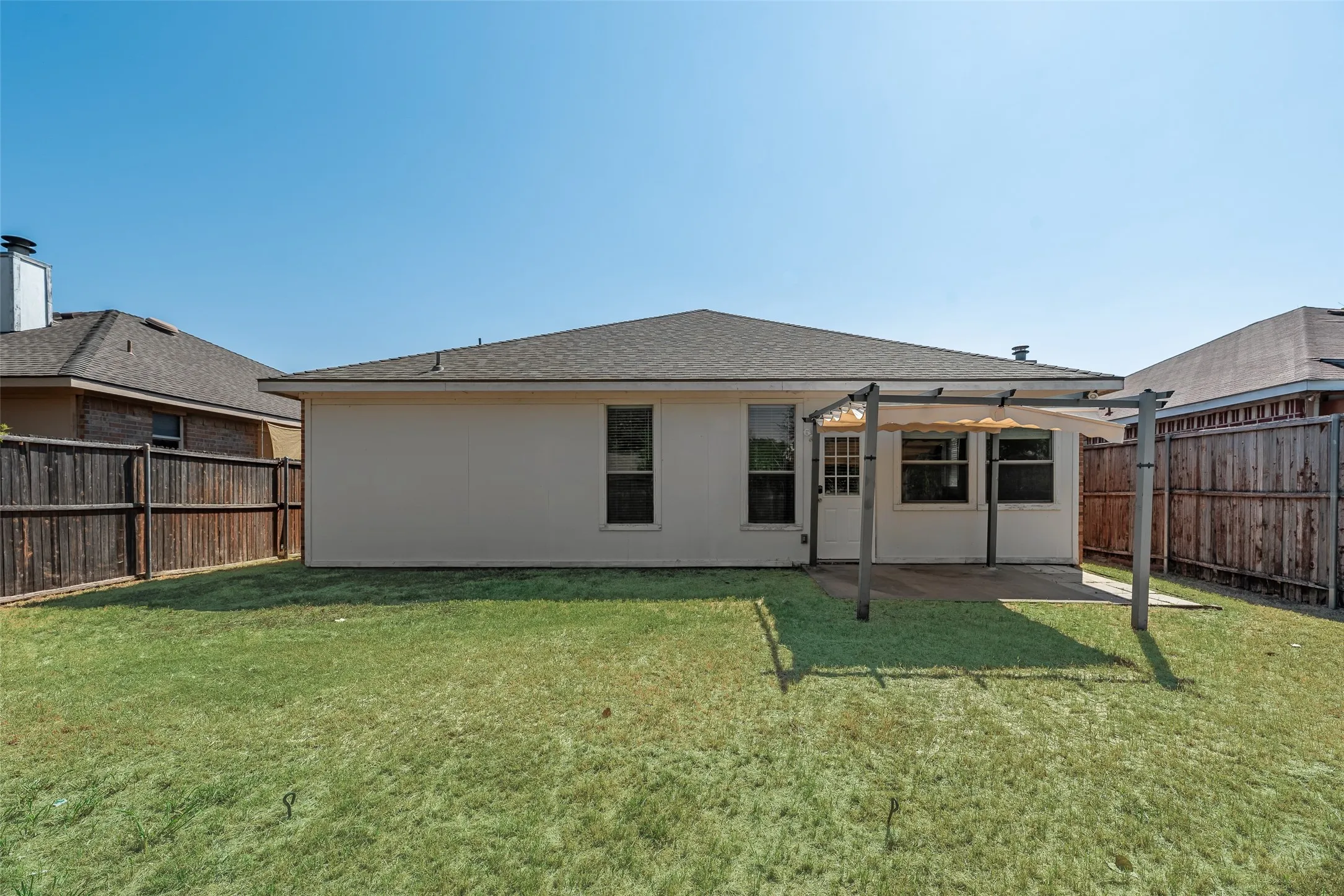 Expansive backyard featuring a manicured lawn, full privacy fencing, and a covered patio with an attached pergola