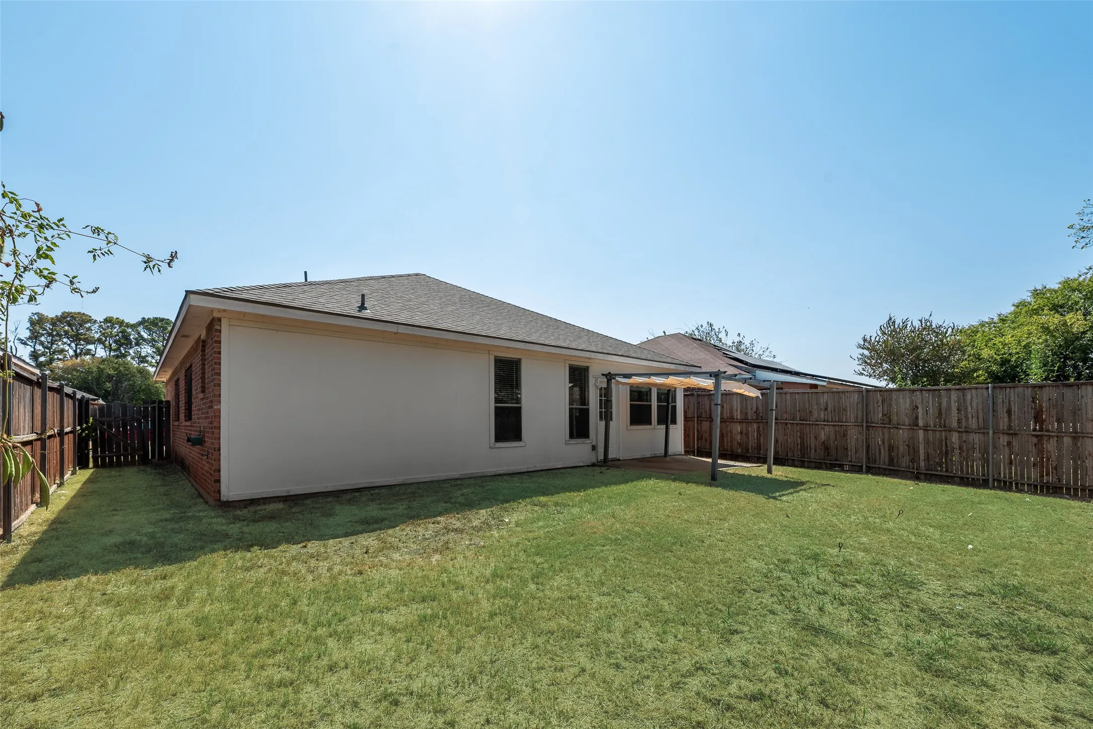 Expansive backyard with a manicured lawn, full privacy fencing, and a built-in pergola