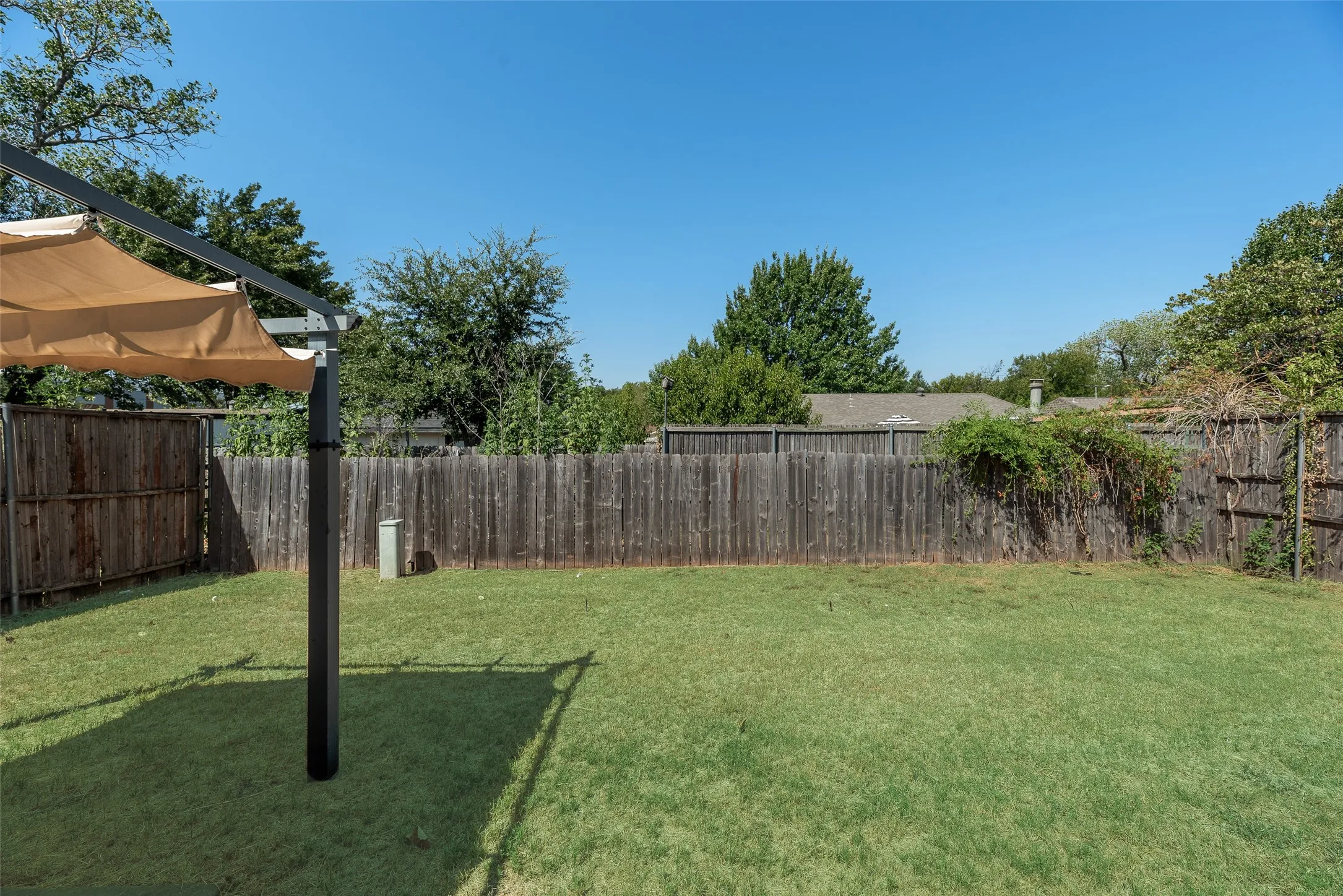 Expansive backyard featuring a pergola with a retractable canopy, wood privacy fencing, and mature perimeter trees