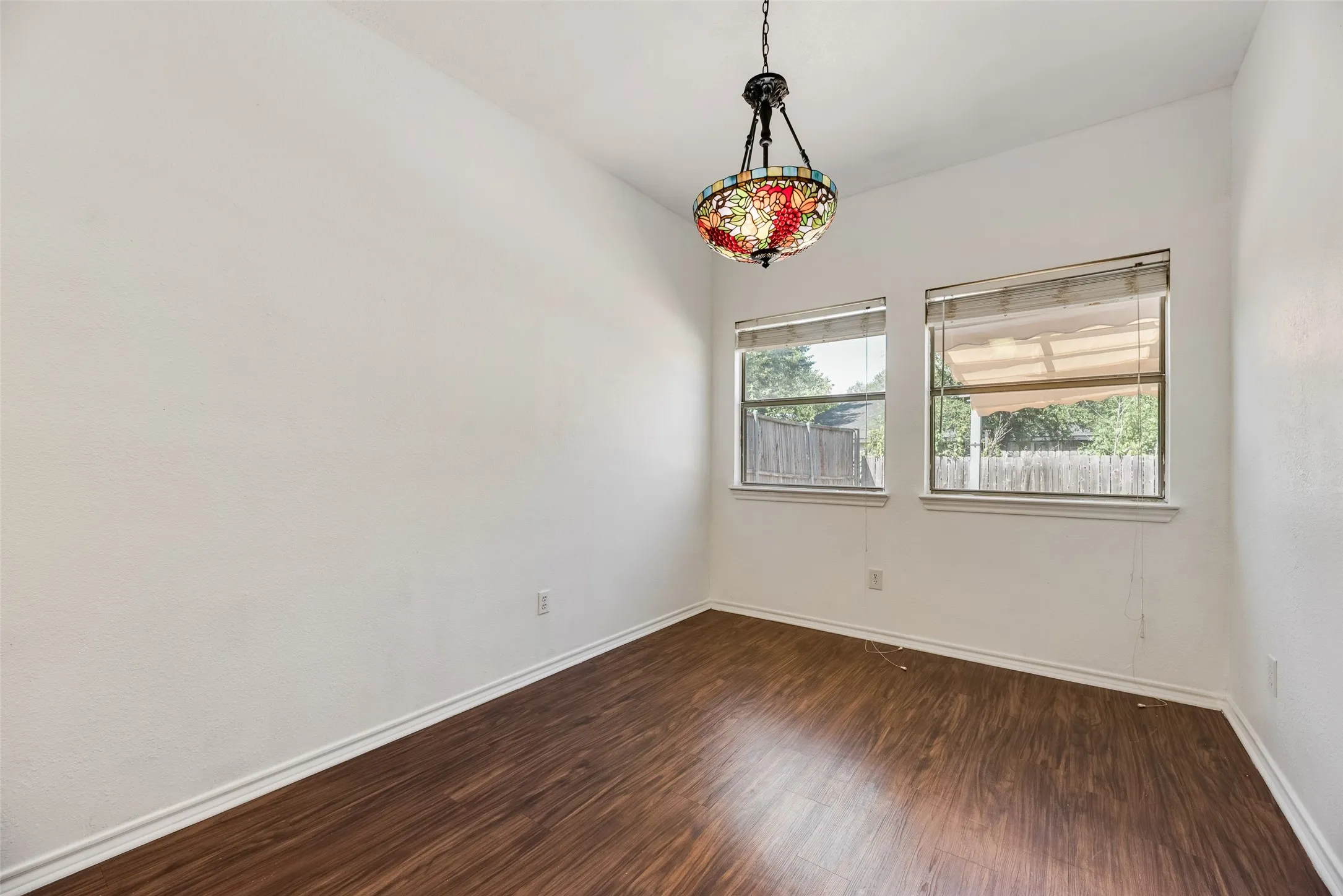 Vaulted ceiling with a decorative hanging light fixture, two windows, and wood-finish flooring