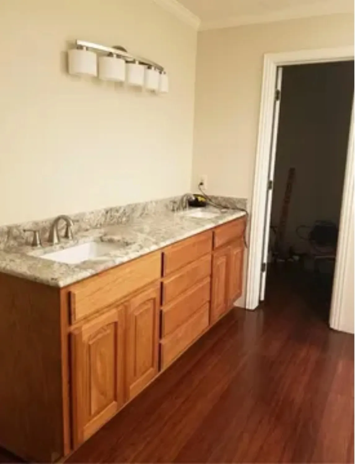 Double vanity with two integrated sinks, stone countertop, wood-finish cabinetry, and wood-finish flooring