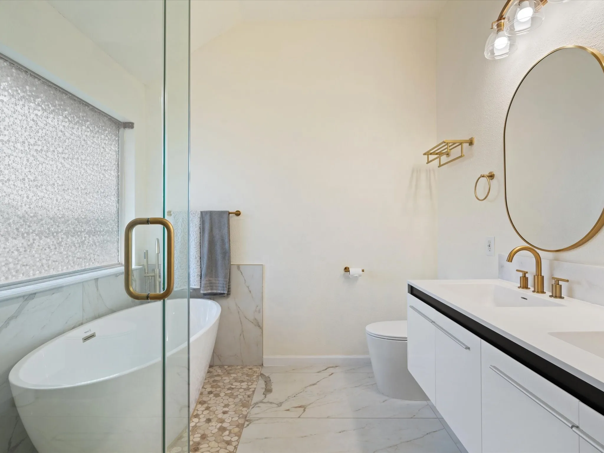 Full bathroom featuring light marble finish floors, a freestanding bath, and double vanity