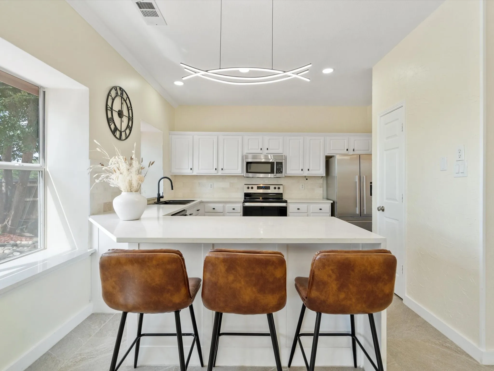 Kitchen featuring tasteful backsplash, stainless steel appliances, a peninsula, white cabinets, and a kitchen breakfast bar