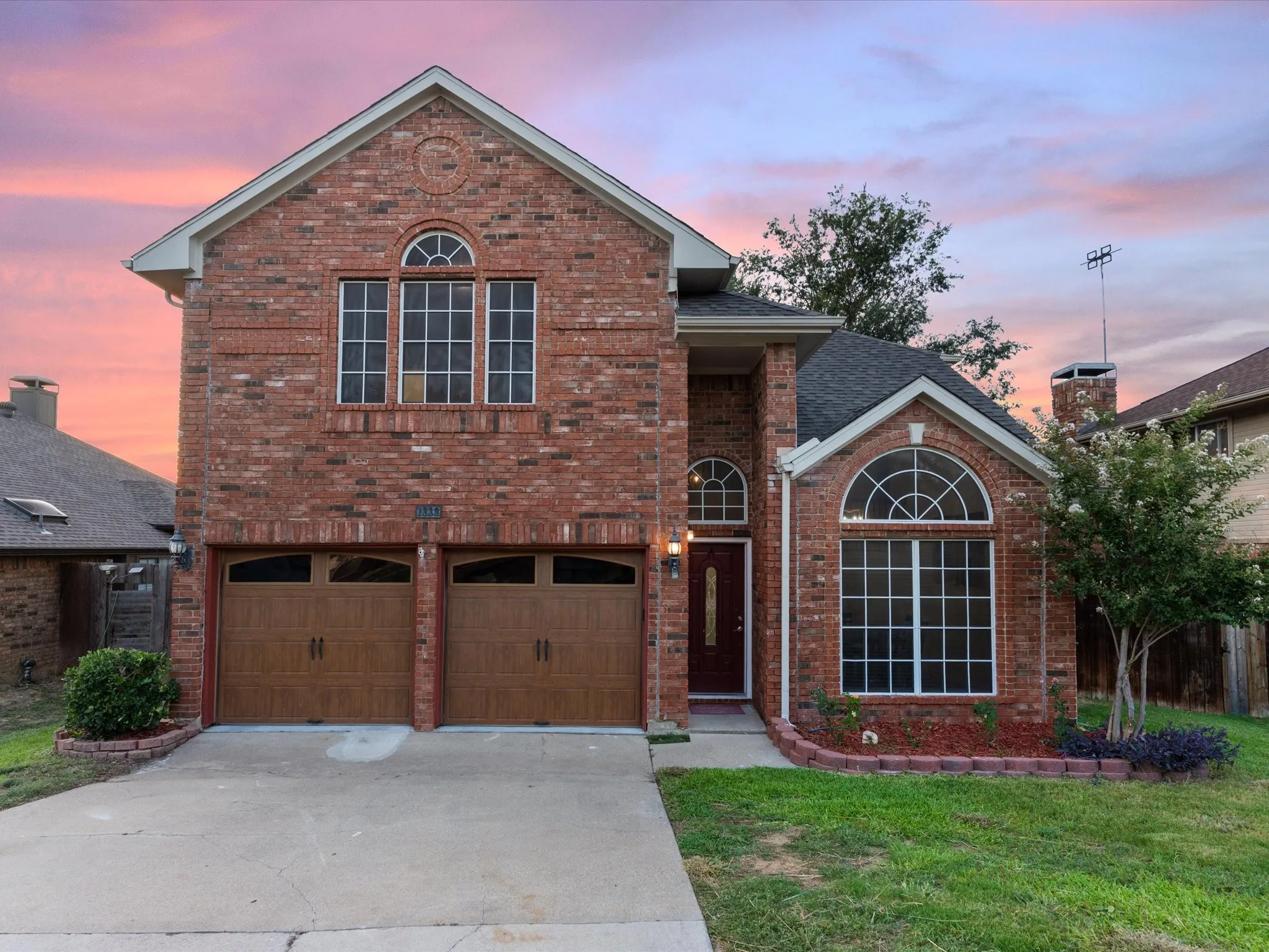 Traditional-style home with brick siding, driveway, an attached garage, a front yard, and roof with shingles