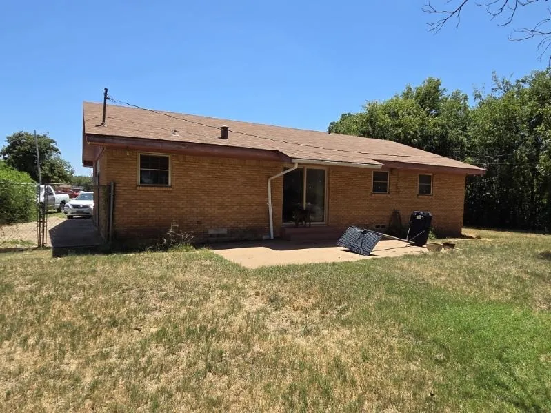 Brick exterior with a shingle roof, rear patio, and a chain-link fence