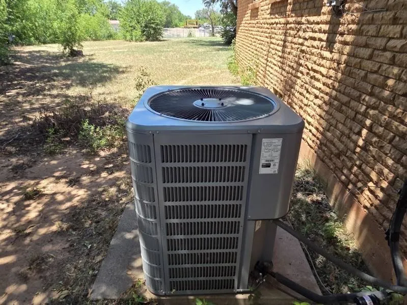 Exterior brick wall with a central air conditioning unit on a concrete pad